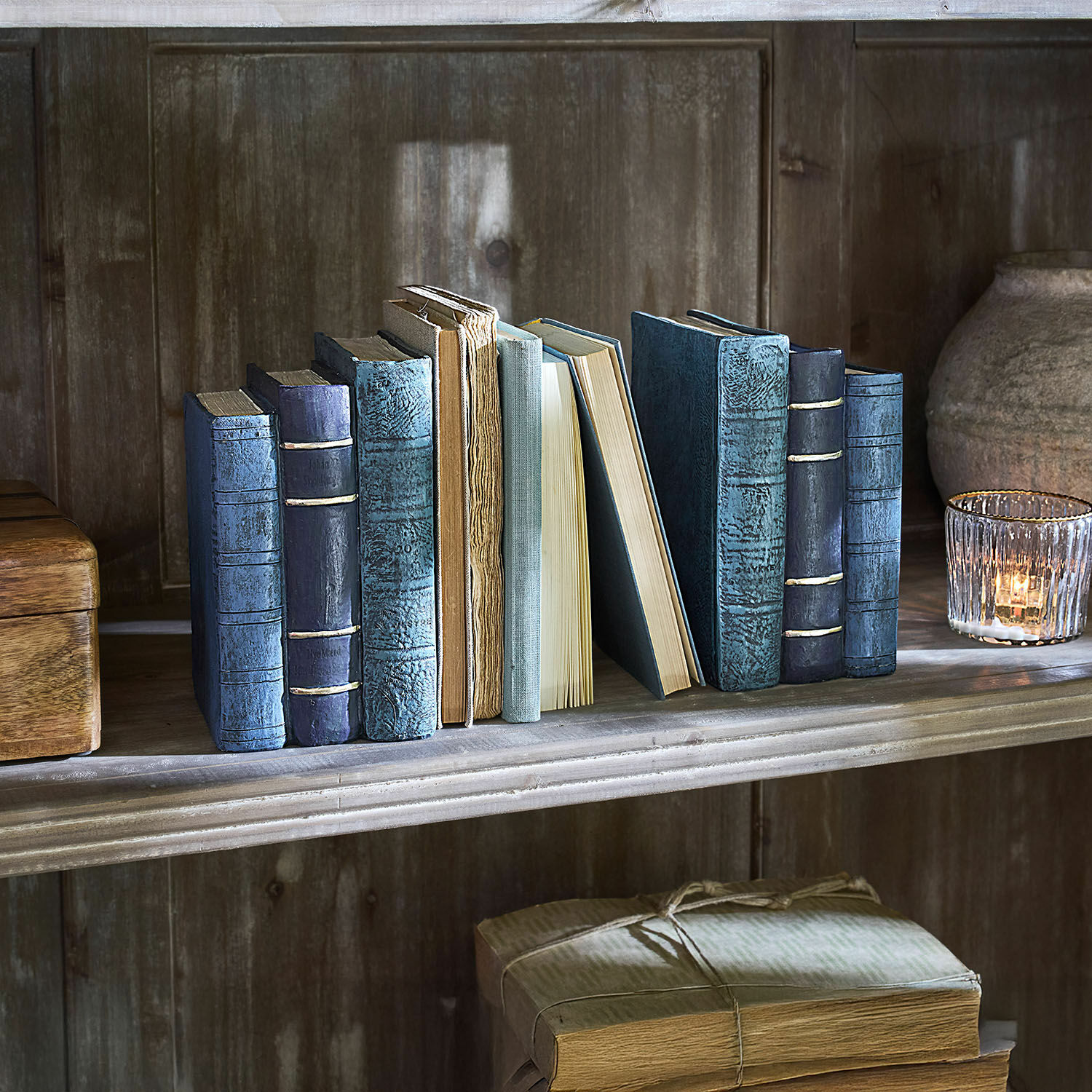Set oude boeken met blauwe en beige kaften op een houten plank naast een windlicht