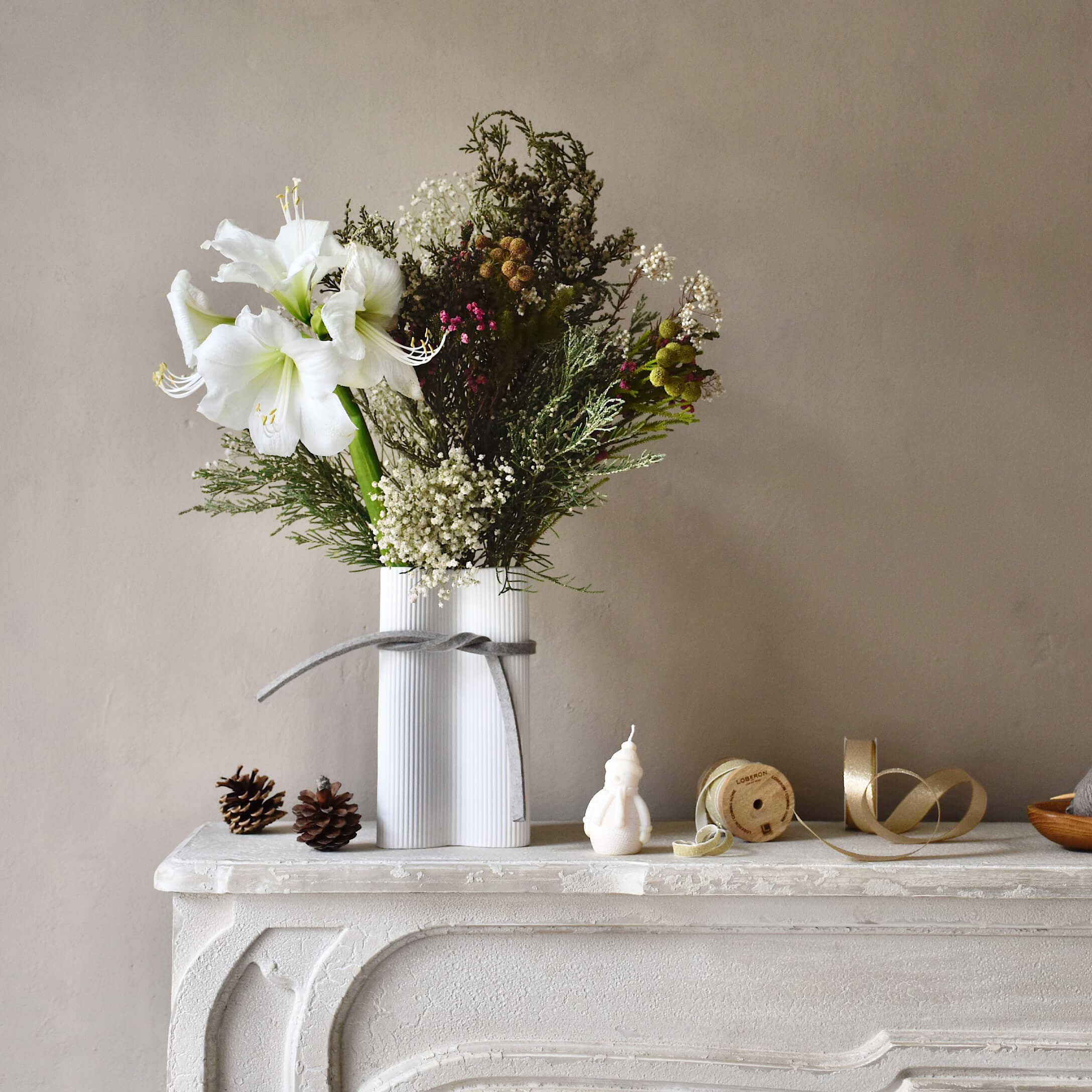 Witte keramische vaas met witte bloemen en groene takken op een decoratieve witte schoorsteen