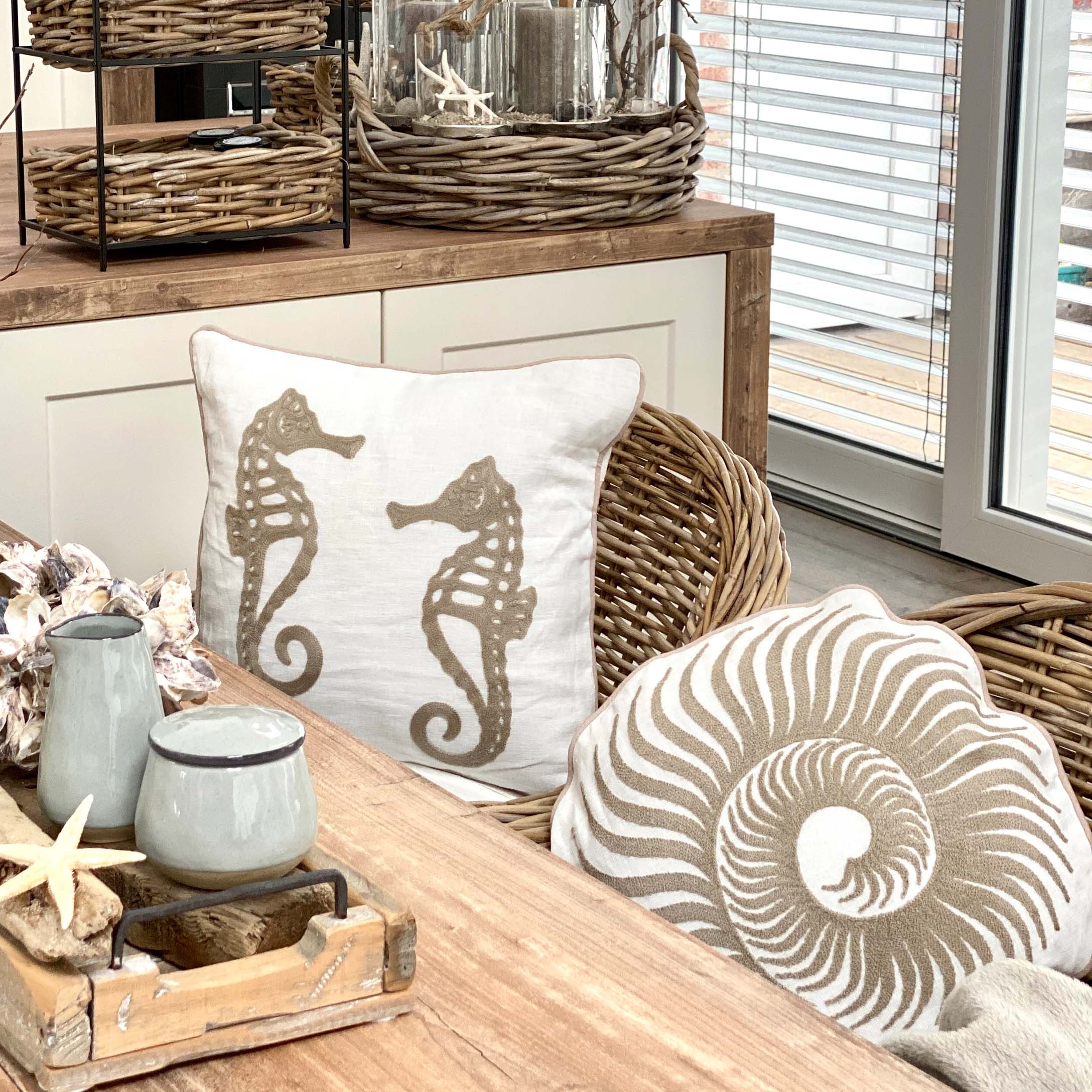Decoratieve kussens met zeepaard- en schelpmotief op rotan stoel in lichte kamer