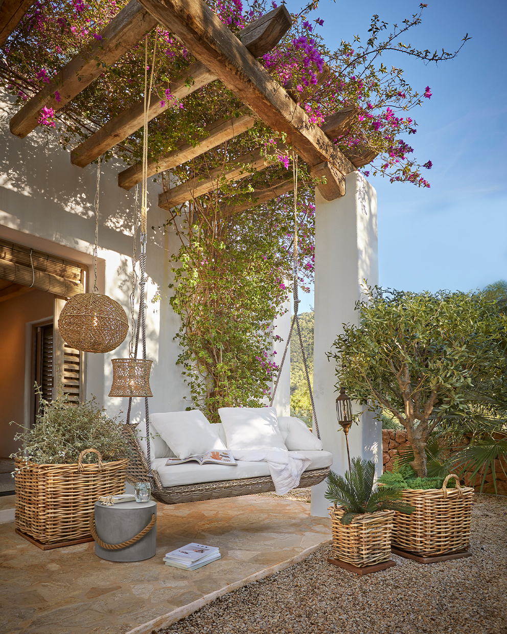Tuin schommel van riet met witte kussens onder een houten pergola met bloemen en planten