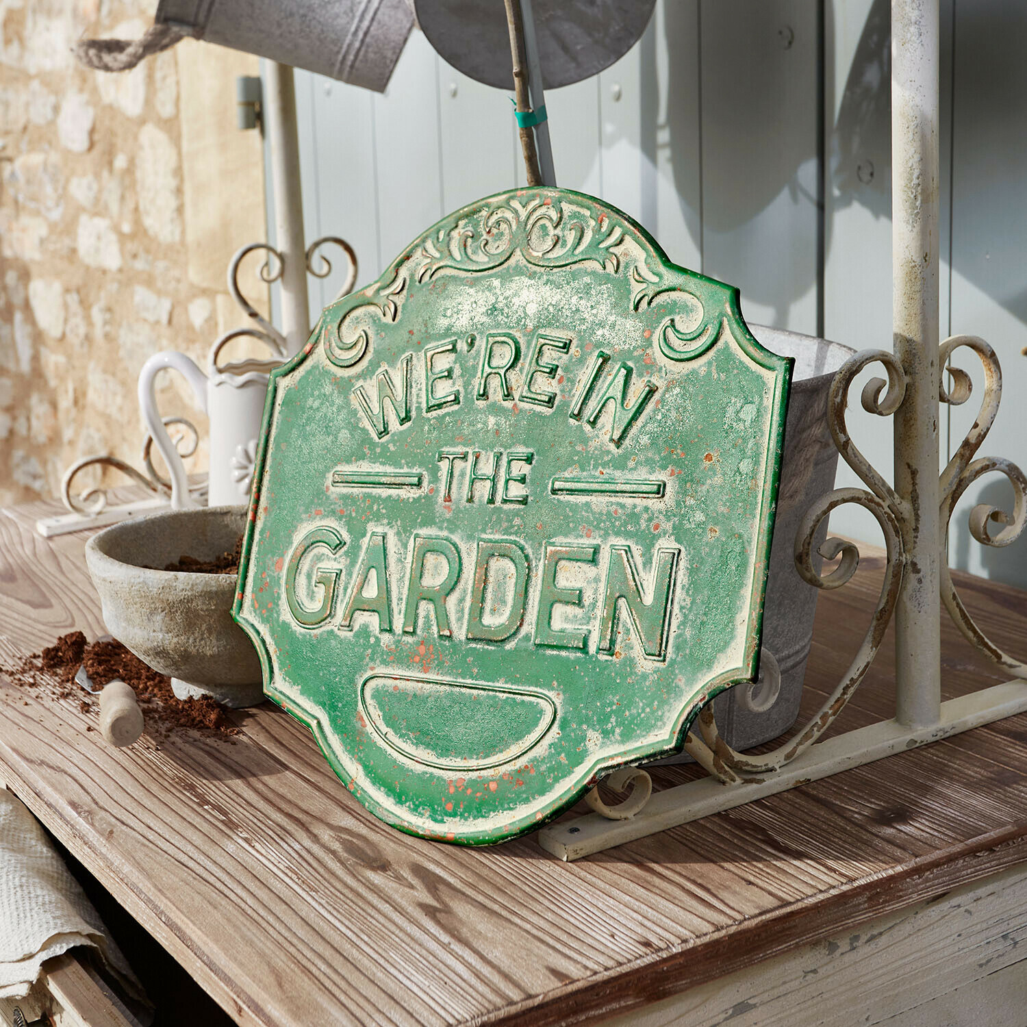 Groen metalen decoratief bord met tekst We're in the Garden op houten tafel in tuin