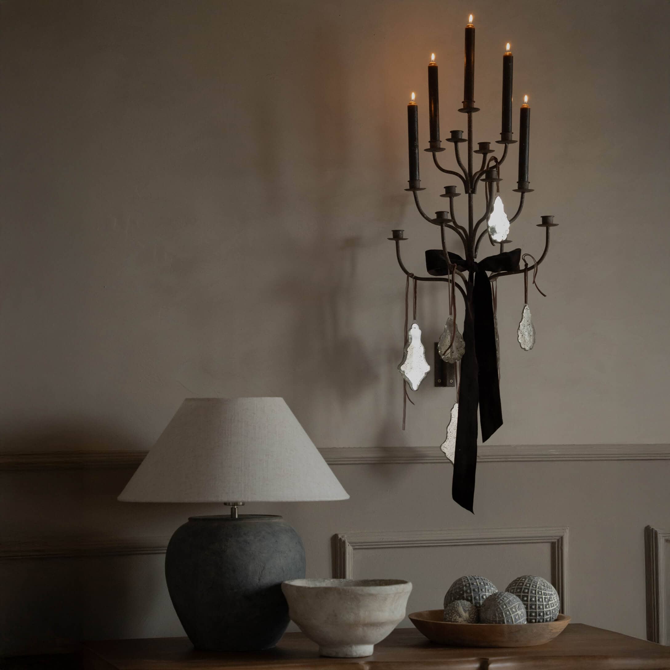 Zwarte metalen wandkandelaar met zwarte strik en hangers, beige tafellamp op houten tafel met decoratie