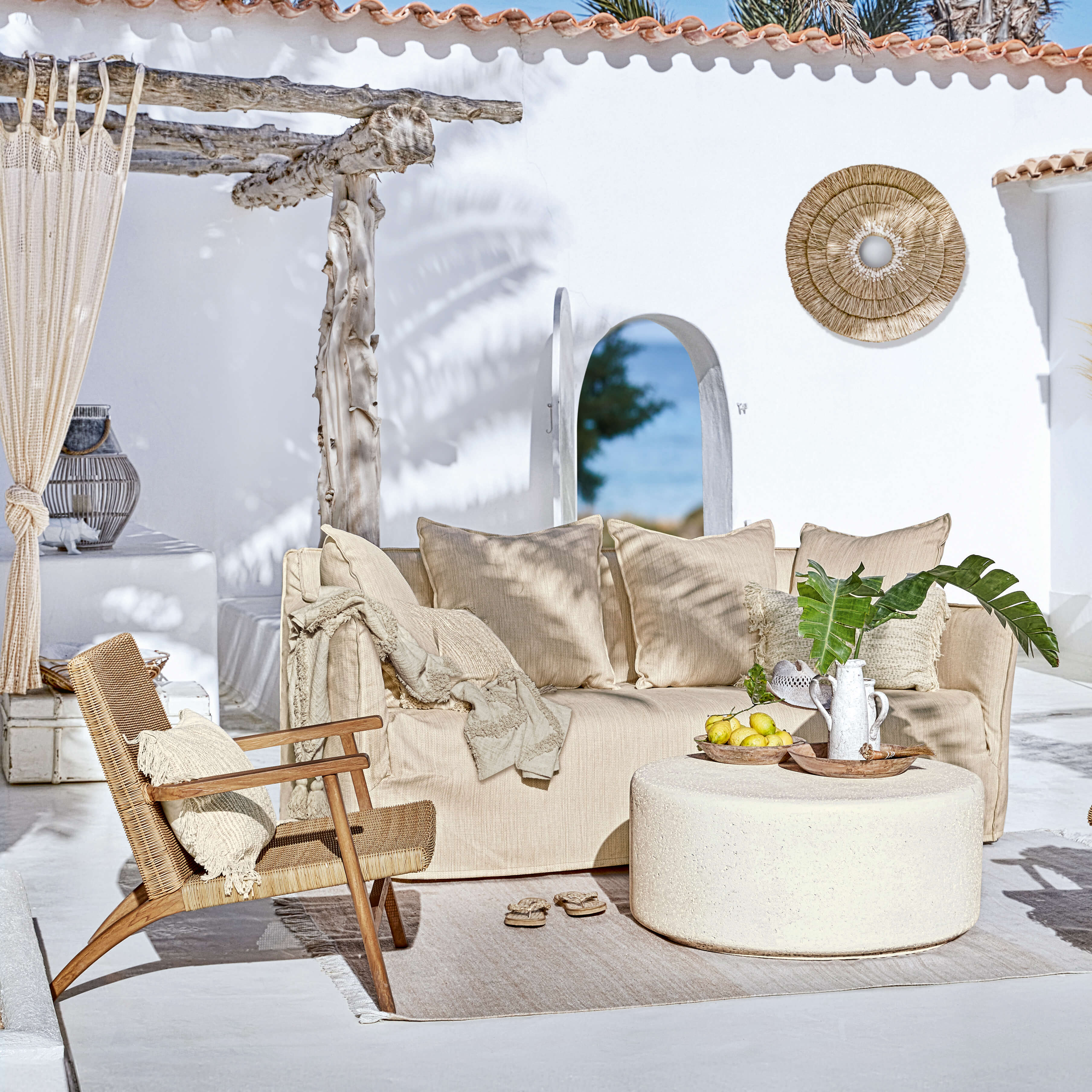 Beige bank en rotan stoel op terras met natuurlijke decoraties en ronde salontafel