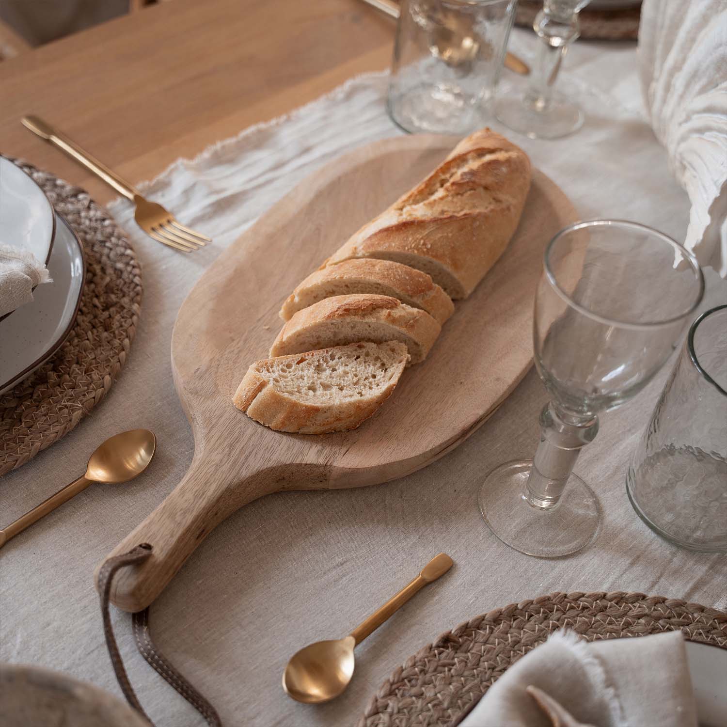 Houten snijplank met gesneden stokbrood op tafel met natuurlijke tafelkleed en gouden bestek