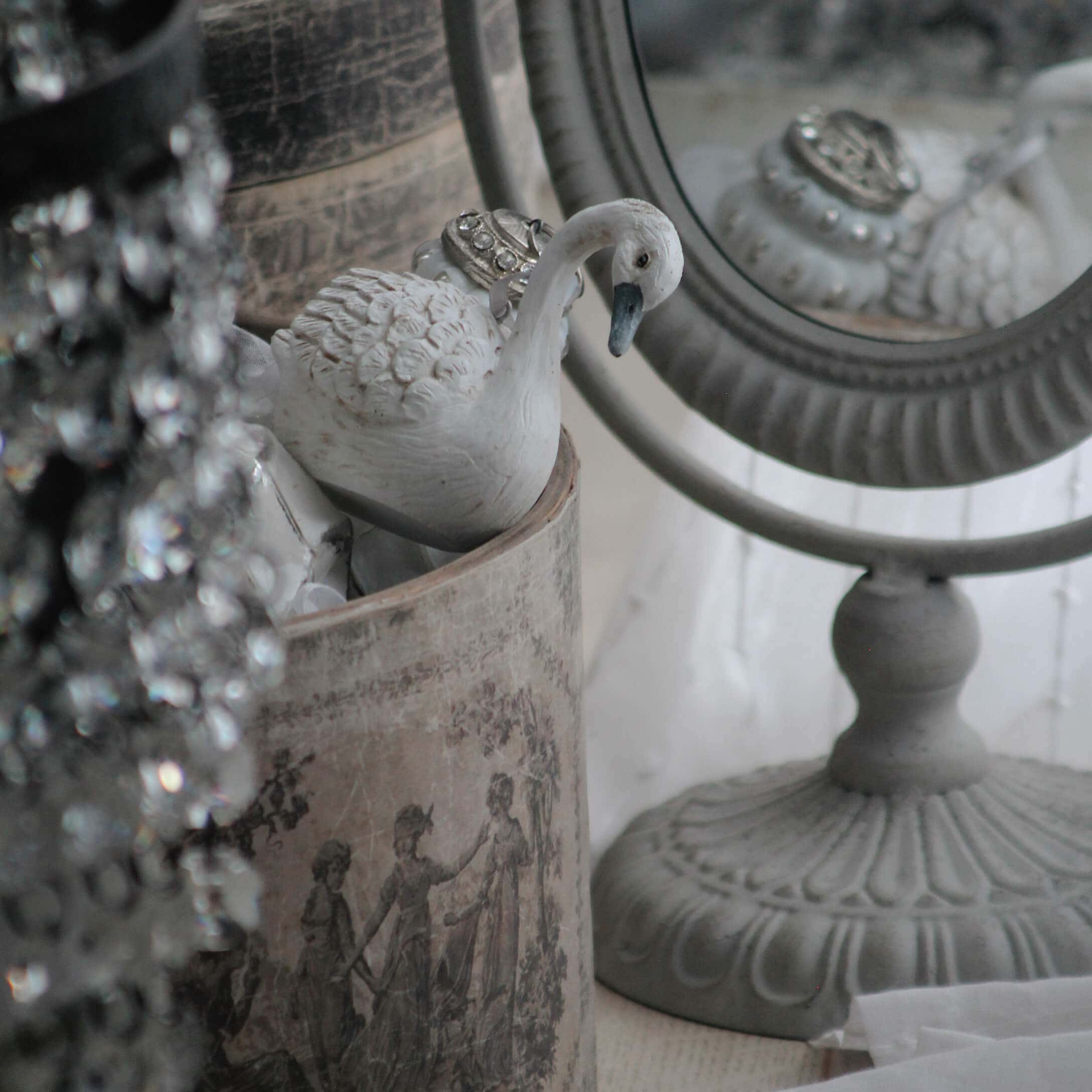 Witte keramische zwaanfiguur naast decoratieve spiegel en vintage houder met klassiek patroon