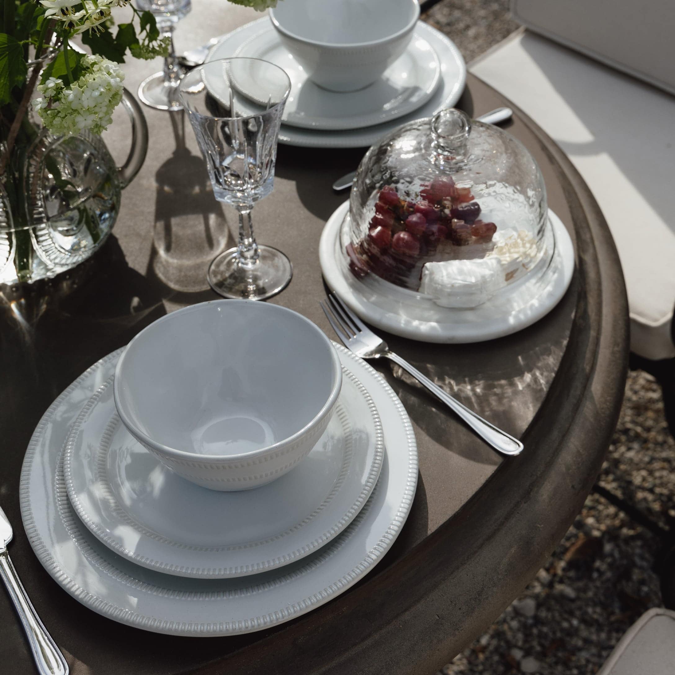 Wit porseleinen servies op bruine tafel met kristallen glas en glazen stolp met druiven