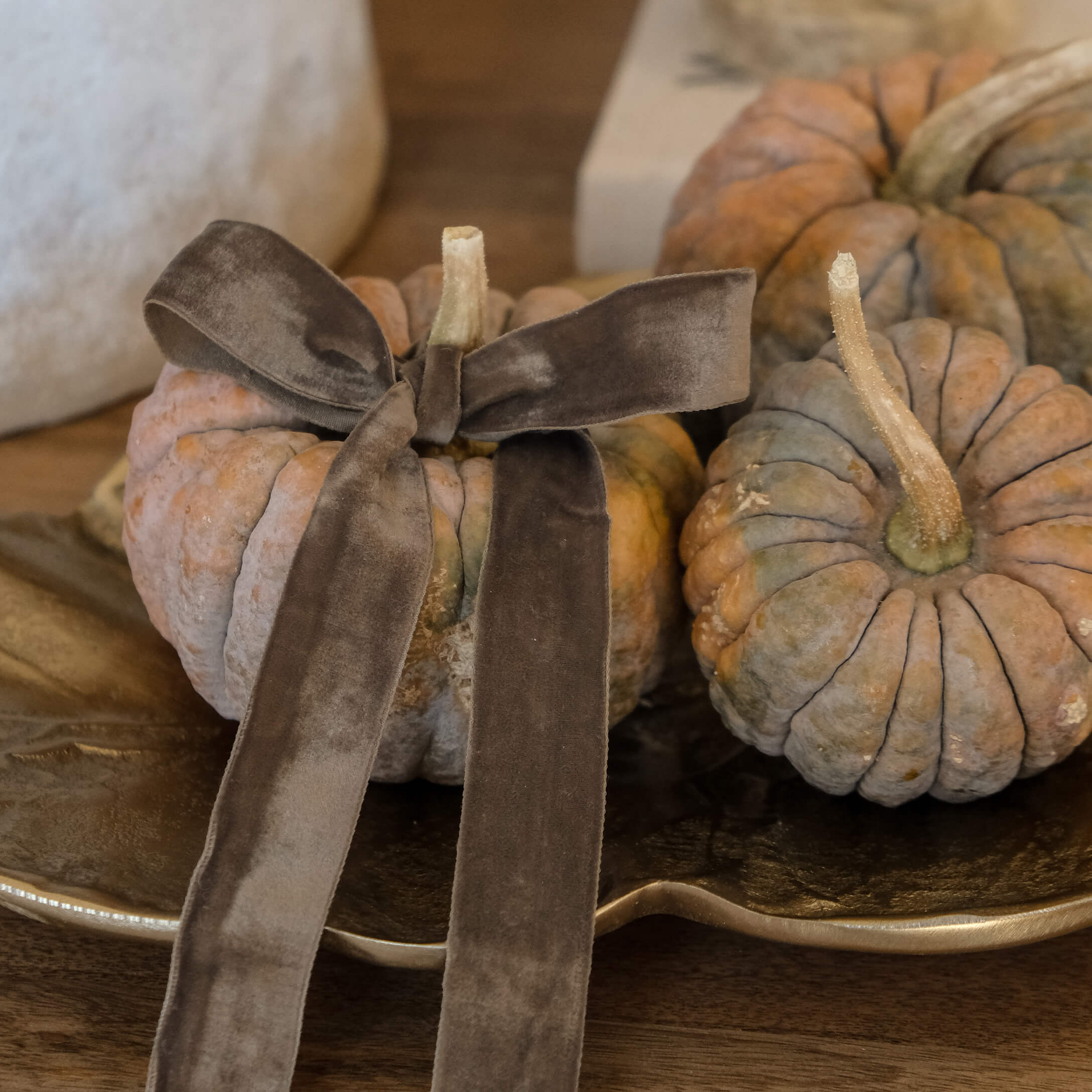 Decoratieve oranje-grijze pompoenen met bruine fluwelen strik op gouden schaal op houten tafel