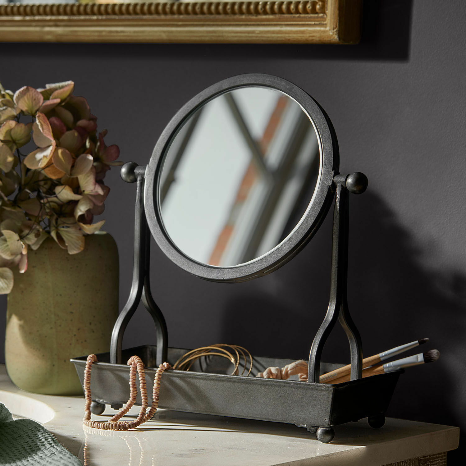 Zwart metalen tafelspiegel met bakje voor sieraden en make-upkwasten op lichte ondergrond