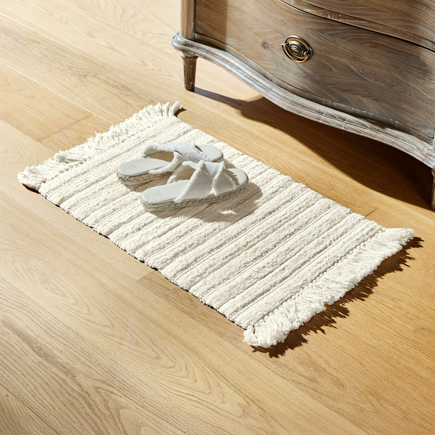 Badmat Dreamyville Crèmekleurig katoenen vloerkleed met franjes op lichte houten vloer met witte slippers, interieurdecoratie