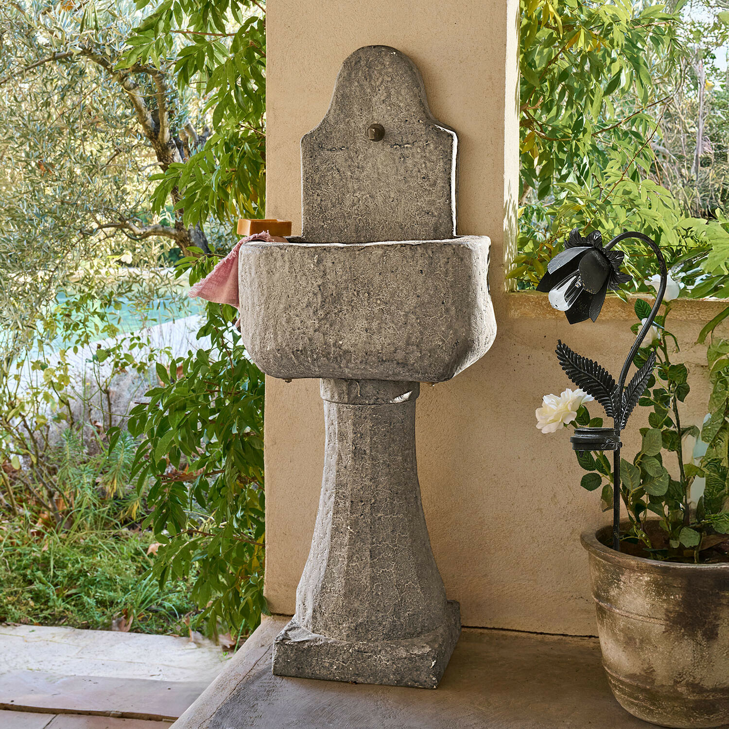Fontein Lurevino Decoratieve grijze stenen tuinwastafel op zuil met natuurlijke afwerking en groene planten op de achtergrond