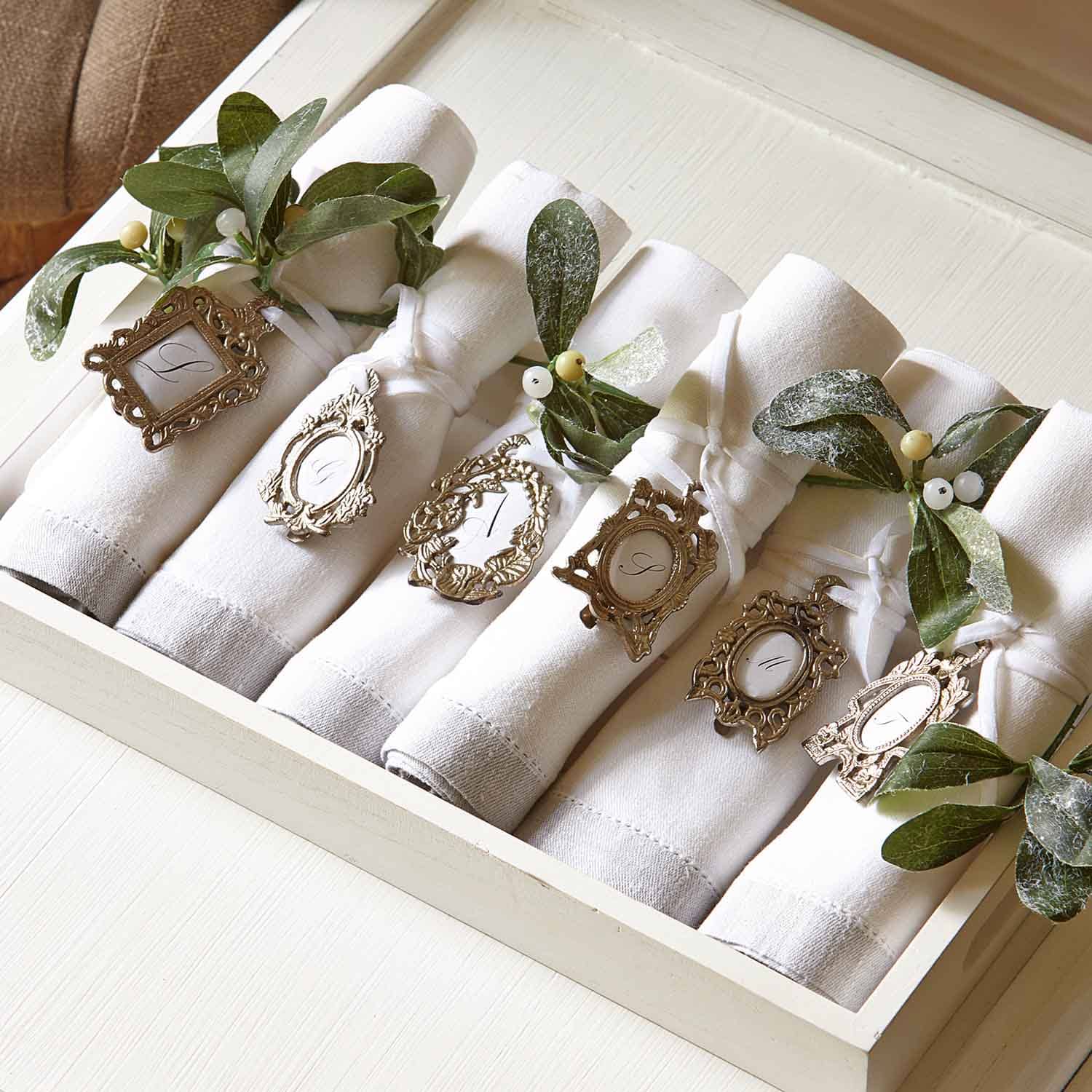 Witte linnen servetten met decoratieve metalen ringen en groene bladeren voor een stijlvolle tafel.