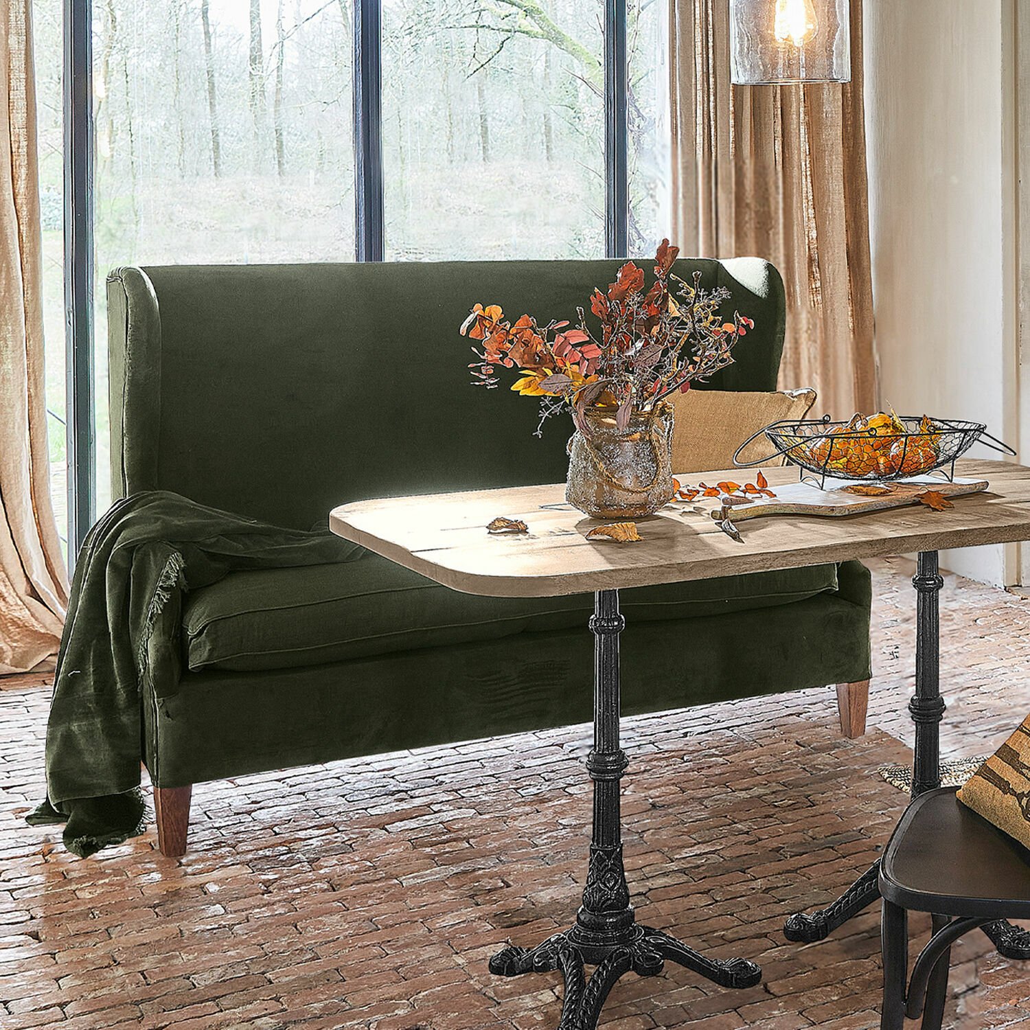 Bank Ombra Groene fluwelen bank bij houten tafel met metalen poten in lichte kamer met bakstenen vloer