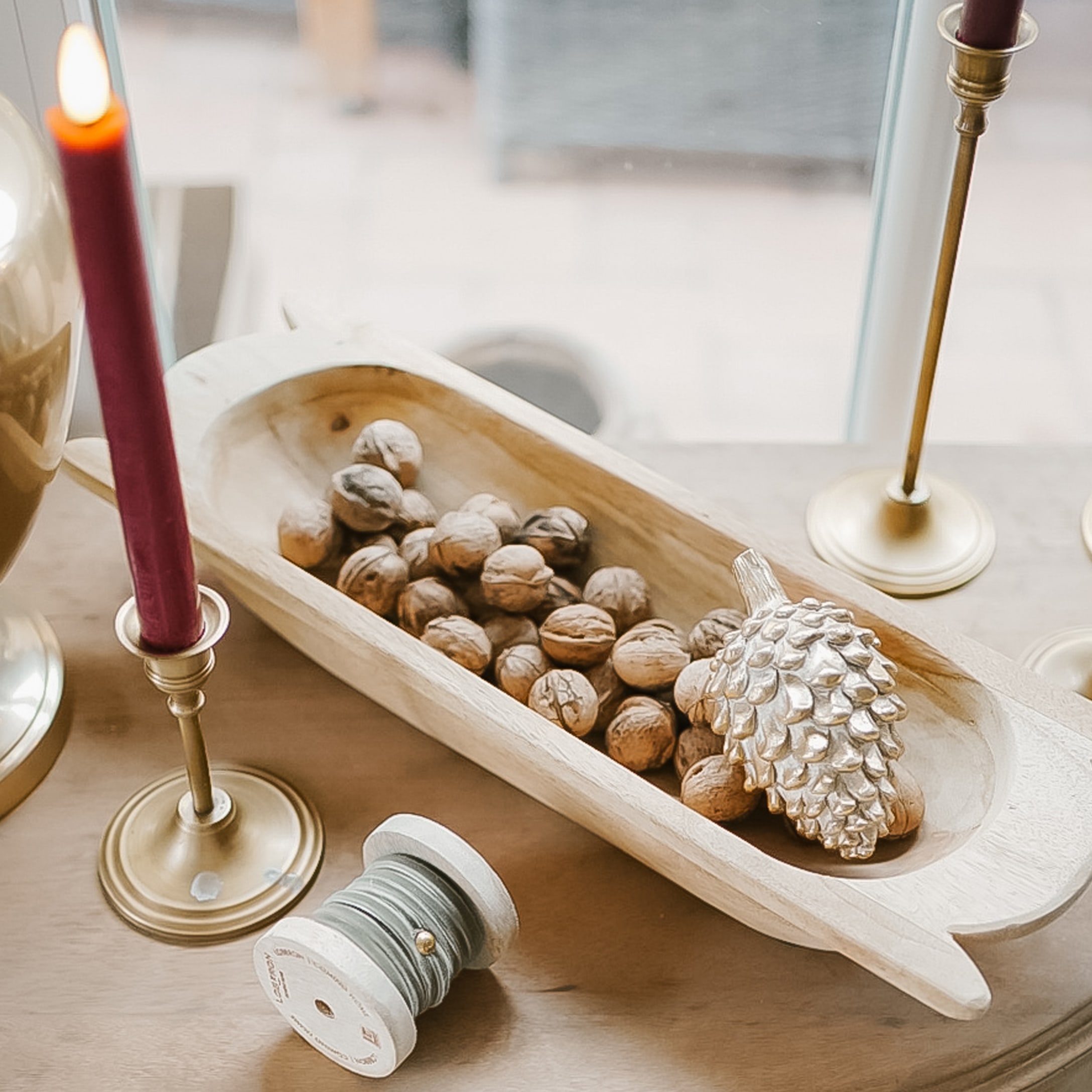 Houten schaal met walnoten en zilveren dennenappel op kersttafel met messing kandelaars