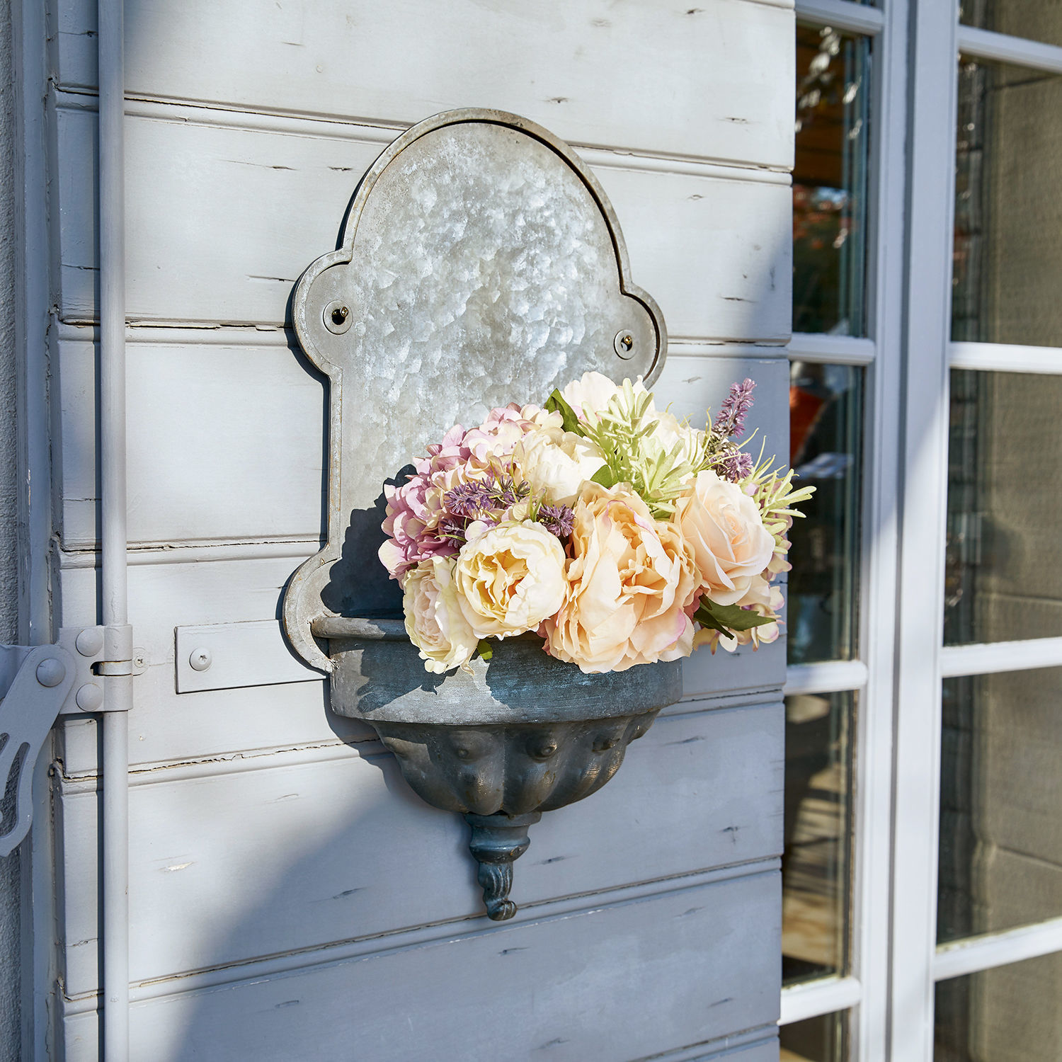 Plantenbak Millieur Metalen wandbloempot met pastelkleurige bloemen aan lichtgrijze buitenmuur