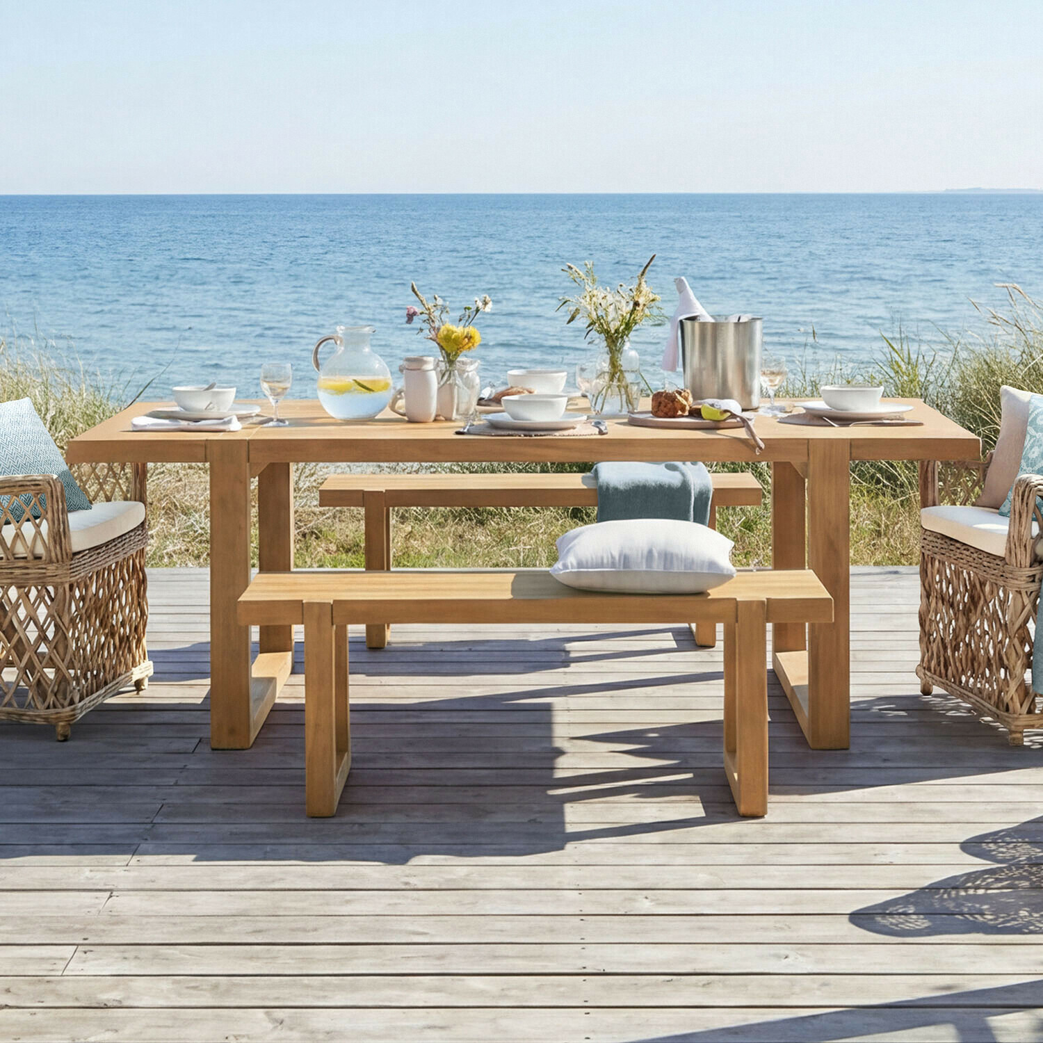 Tafel Halinor Houten tuintafel met banken en rotan stoelen aan zee, gedekt met servies en bloemen