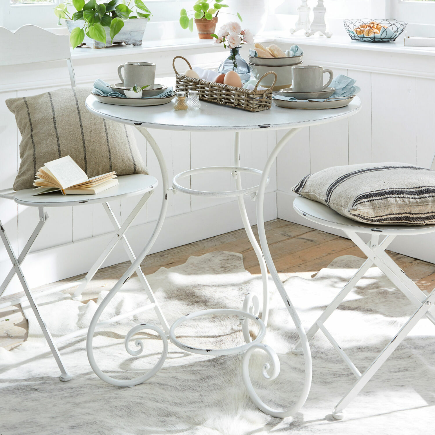 Tafel Iteuil Witte metalen tafel met twee inklapbare stoelen en decoratieve kussens in lichte kamer