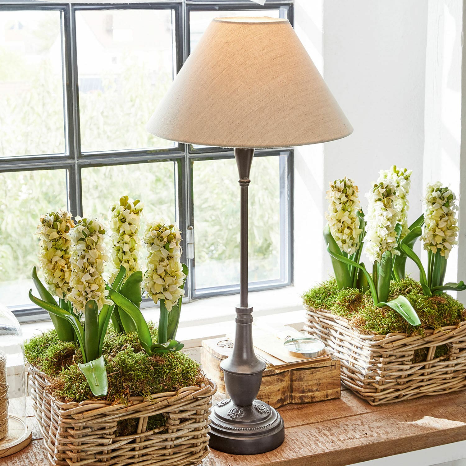 Tafellamp Barnwell Tafellamp met metalen voet en beige kap naast rieten manden met witte bloemen en mos