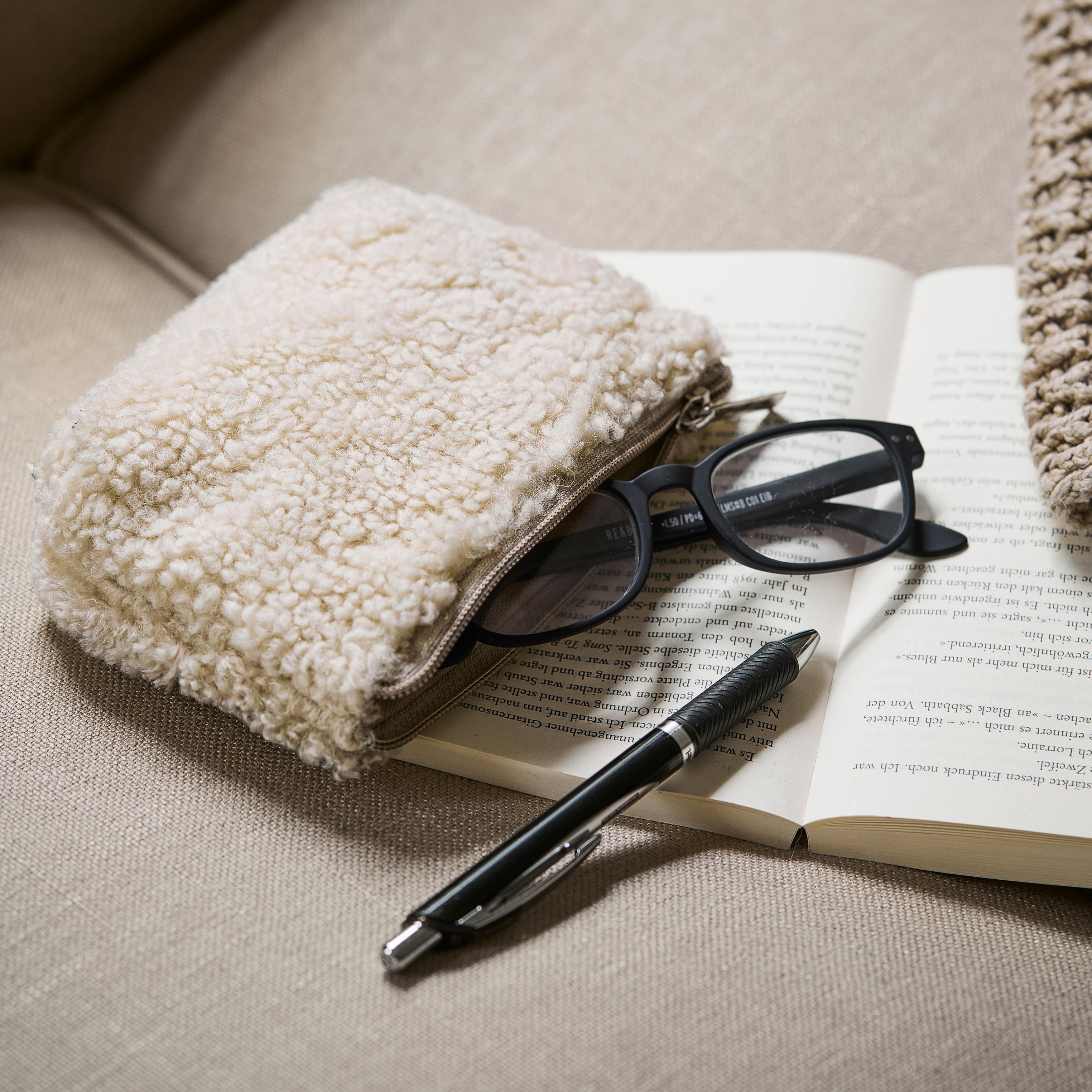 Beige zachte make-uptas op bank naast bril en pen op open boek