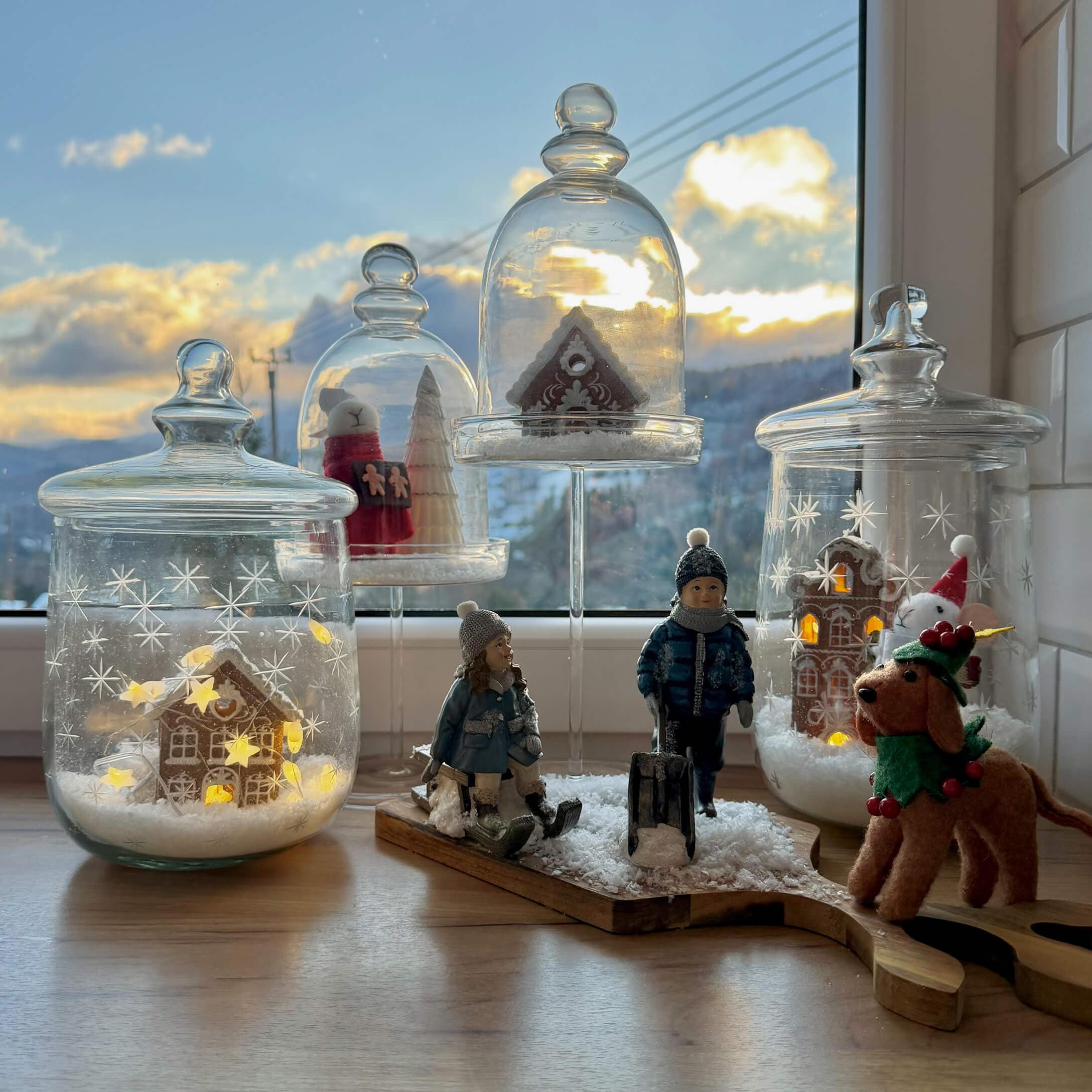 Kerstdecoratie met kinderfiguren, hond en peperkoekhuisjes onder glazen stolpen op vensterbank