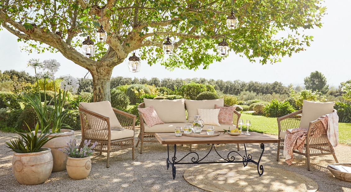 Tuinmeubelset met beige kussens en houten tafel onder een boom op het terras
