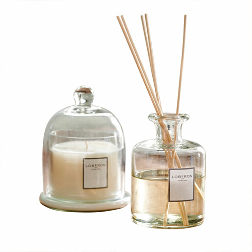 Glazen geurverspreider en kaars onder glazen stolp in neutrale kleuren voor aromatherapie