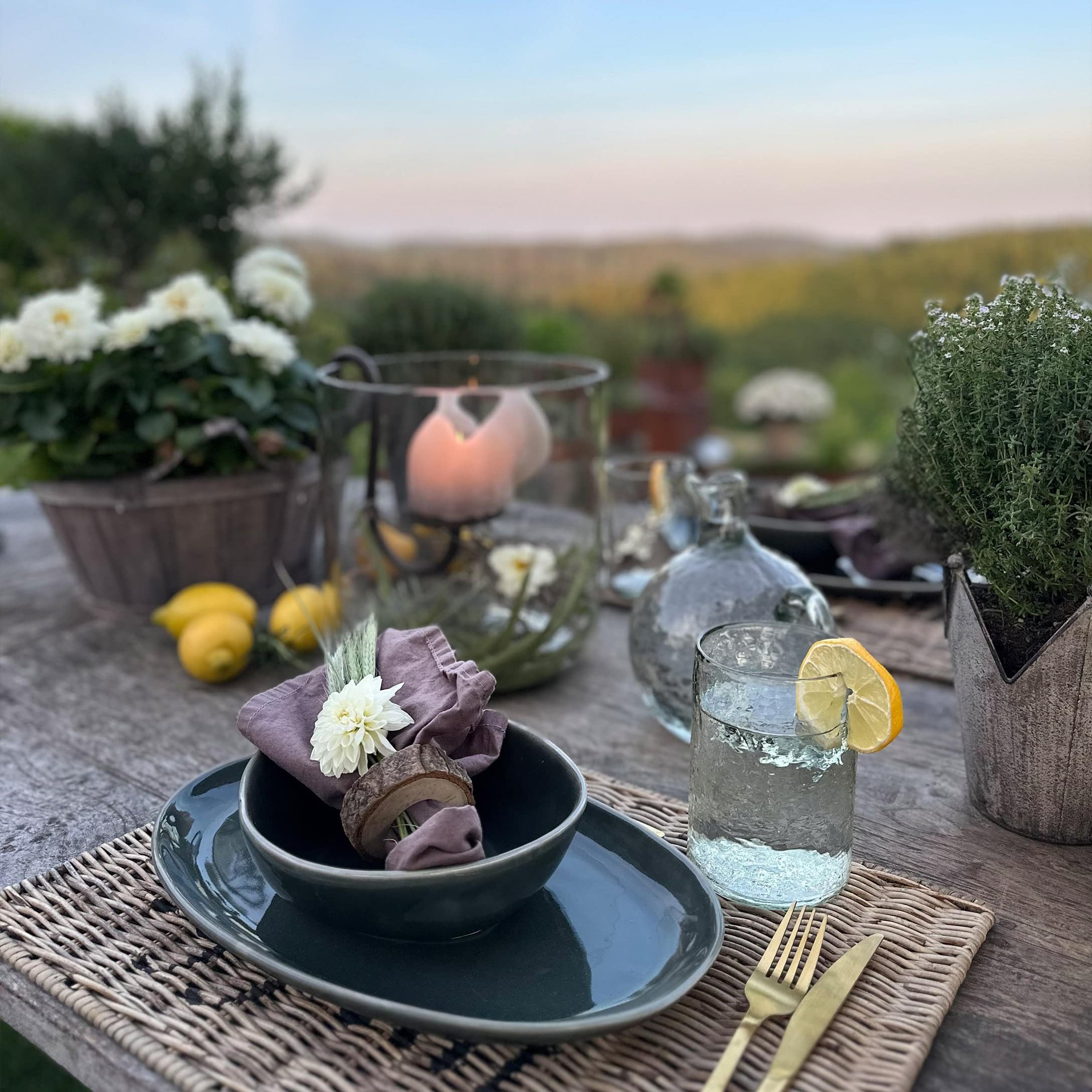 Rustieke tafel met donker keramiek, linnen servet en glas water met citroen buiten