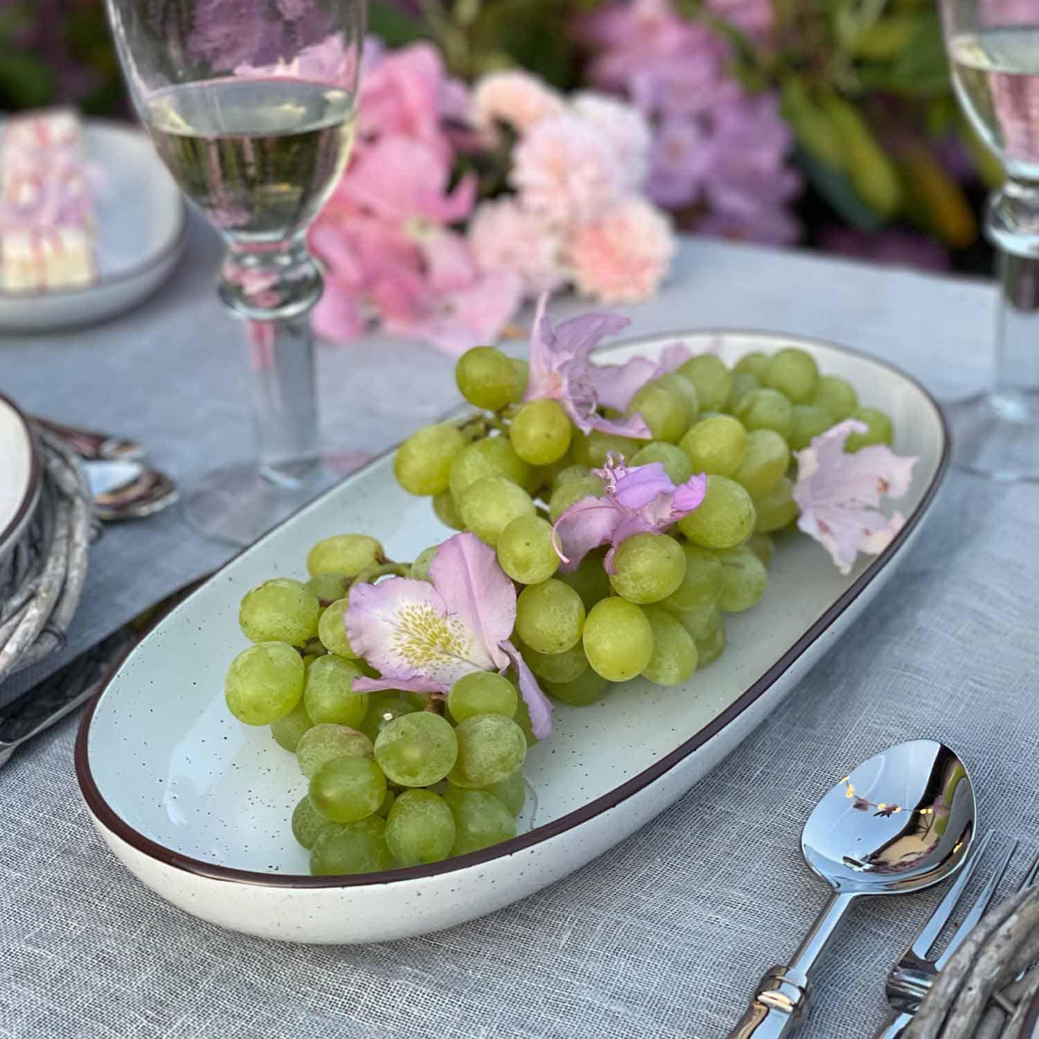 Groene druiven met roze bloemen op een wit keramisch bord op een grijze tafelkleed