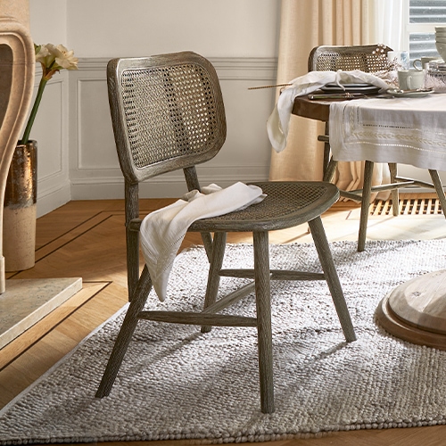 Stoel van hout en riet in natuurlijke kleur op tapijt in lichte woonkamer met gedekte tafel