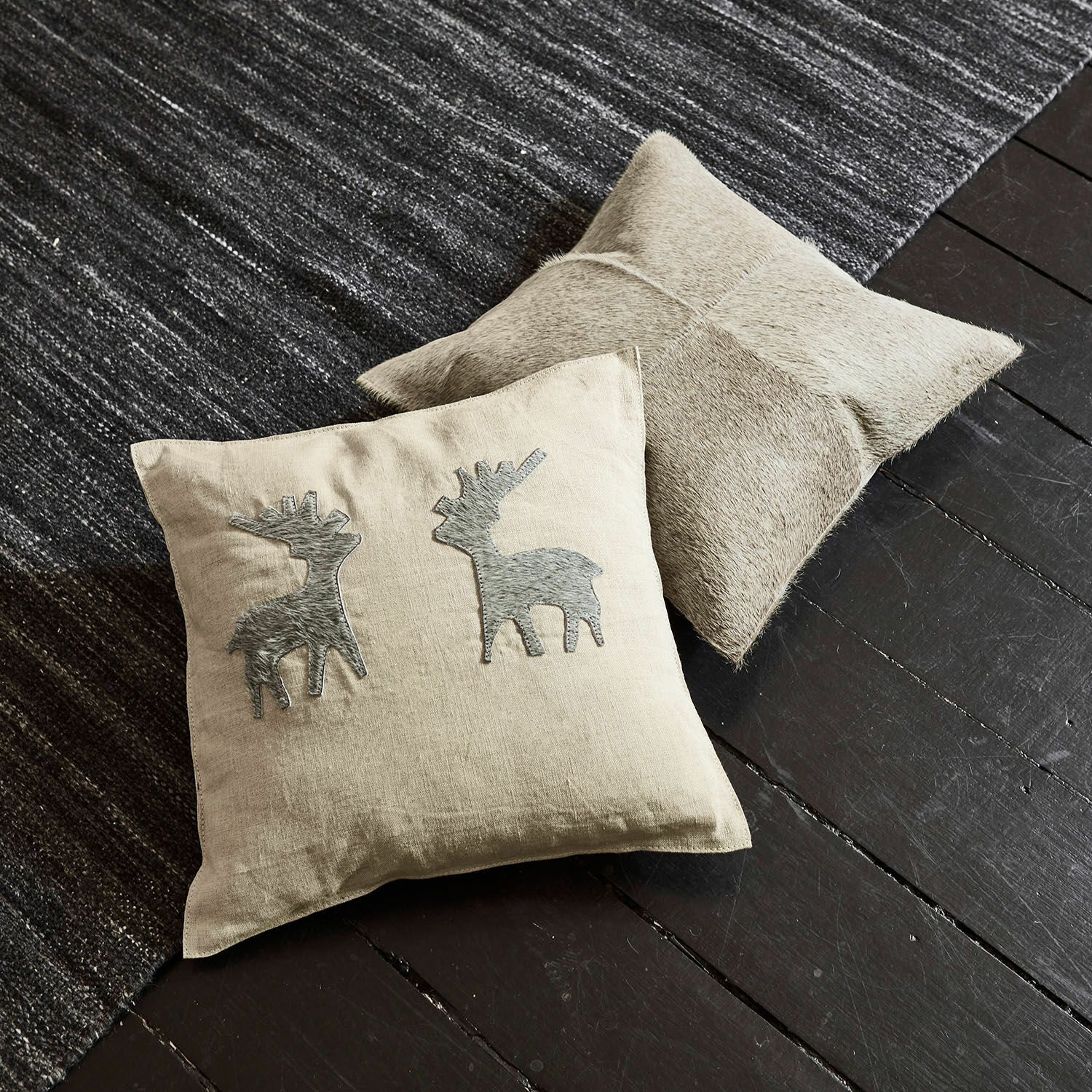 Kussenhoes set van 2 Beaupuy Beige linnen kussen met grijze hertapplicaties en lichtbruin leren kussen op donkere vloer en tapijt