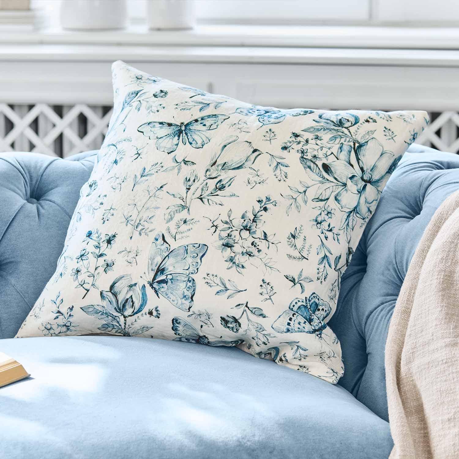 Decoratief katoenen kussen met blauw vlinder- en bloemenpatroon op lichte achtergrond op blauwe bank