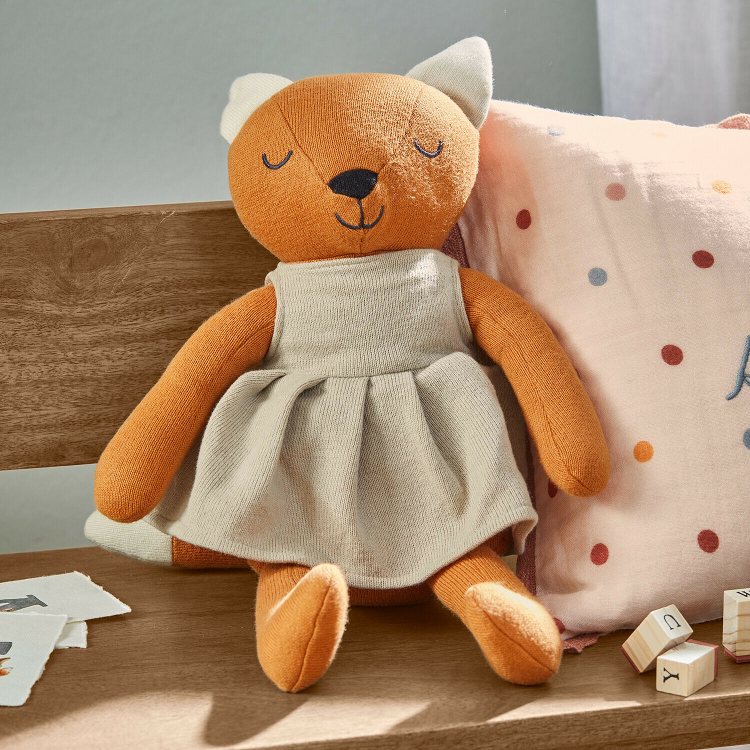 Knuffeltje Fuzzlin Zachte oranje pluche vos in beige jurk zittend op houten bank met kussen en houten blokken