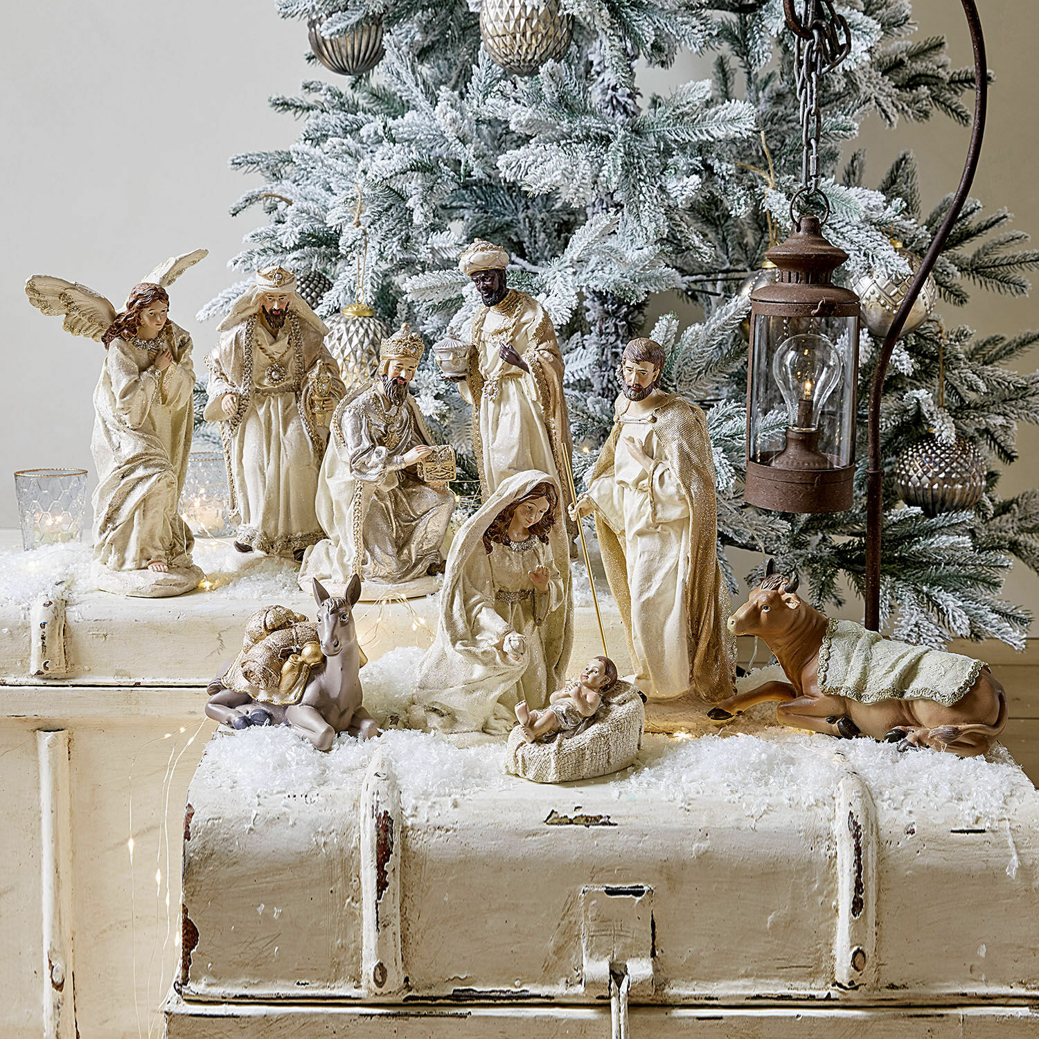 Kerststalfiguren in crèmekleuren voor besneeuwde kerstboom en rustieke lantaarn