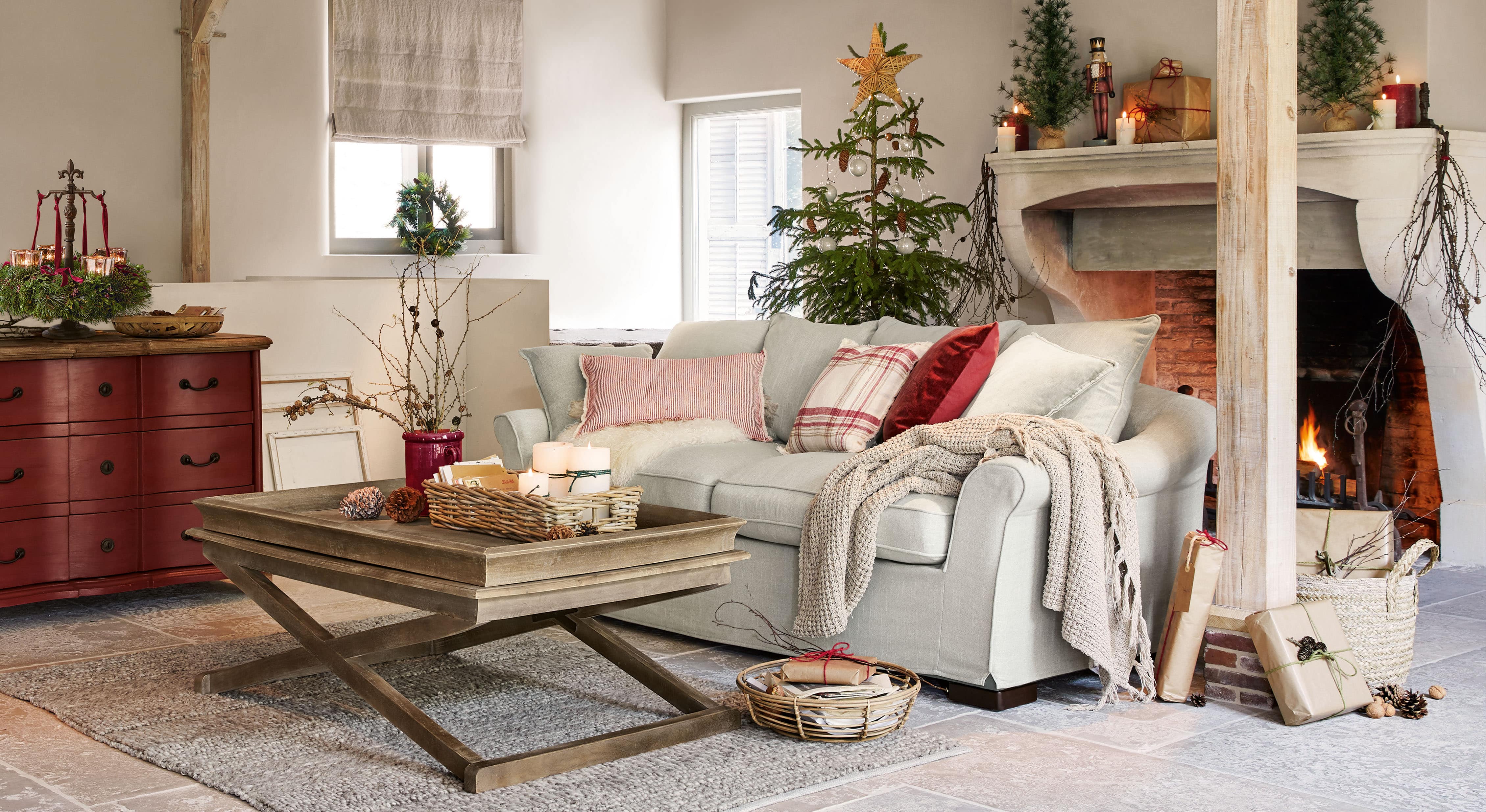Gezellige woonkamer met lichtgrijze bank, houten salontafel en kerstdecoratie met boom en brandende open haard