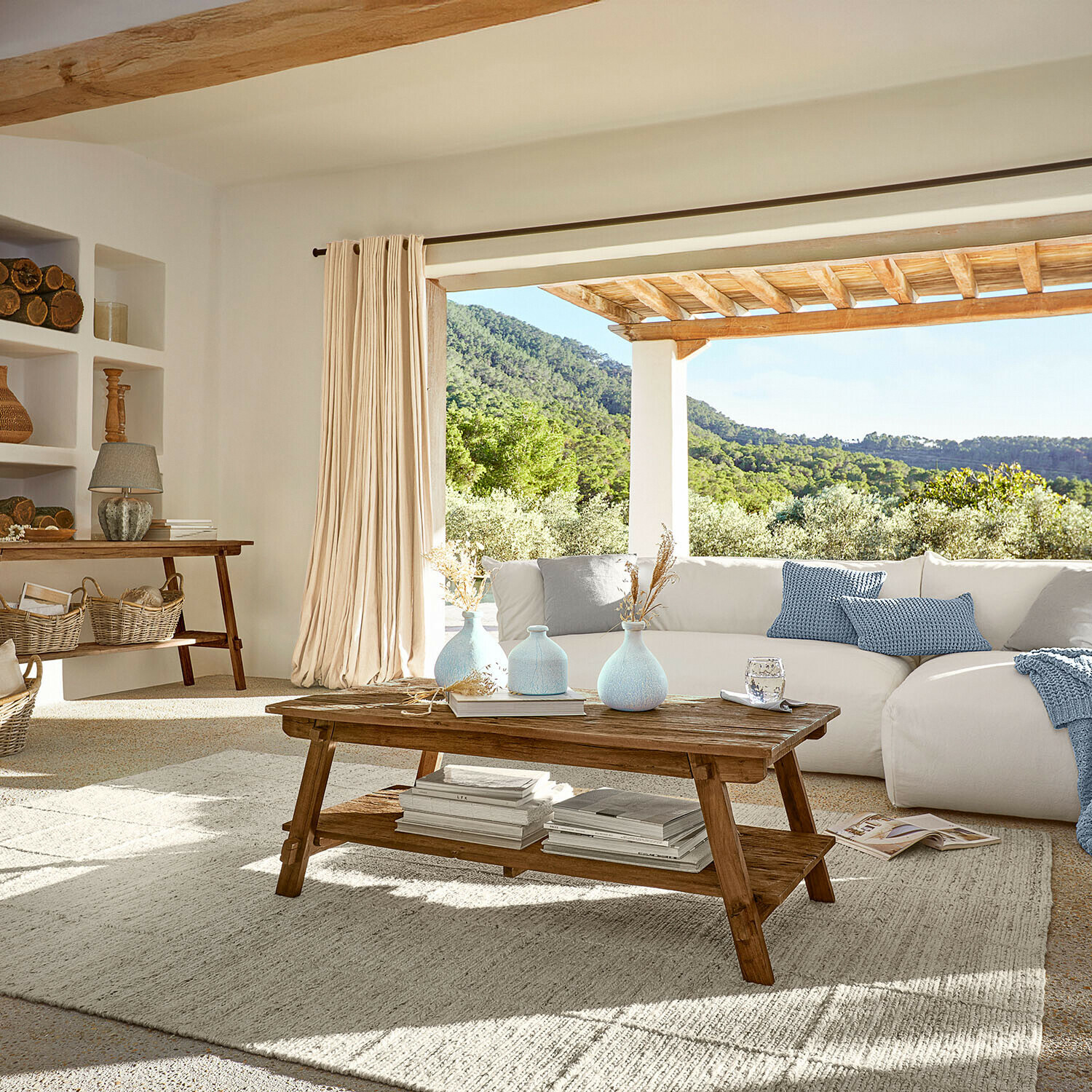 Woonkamer met houten salontafel en witte bank met blauwe kussens, natuurlijk licht en warme sfeer