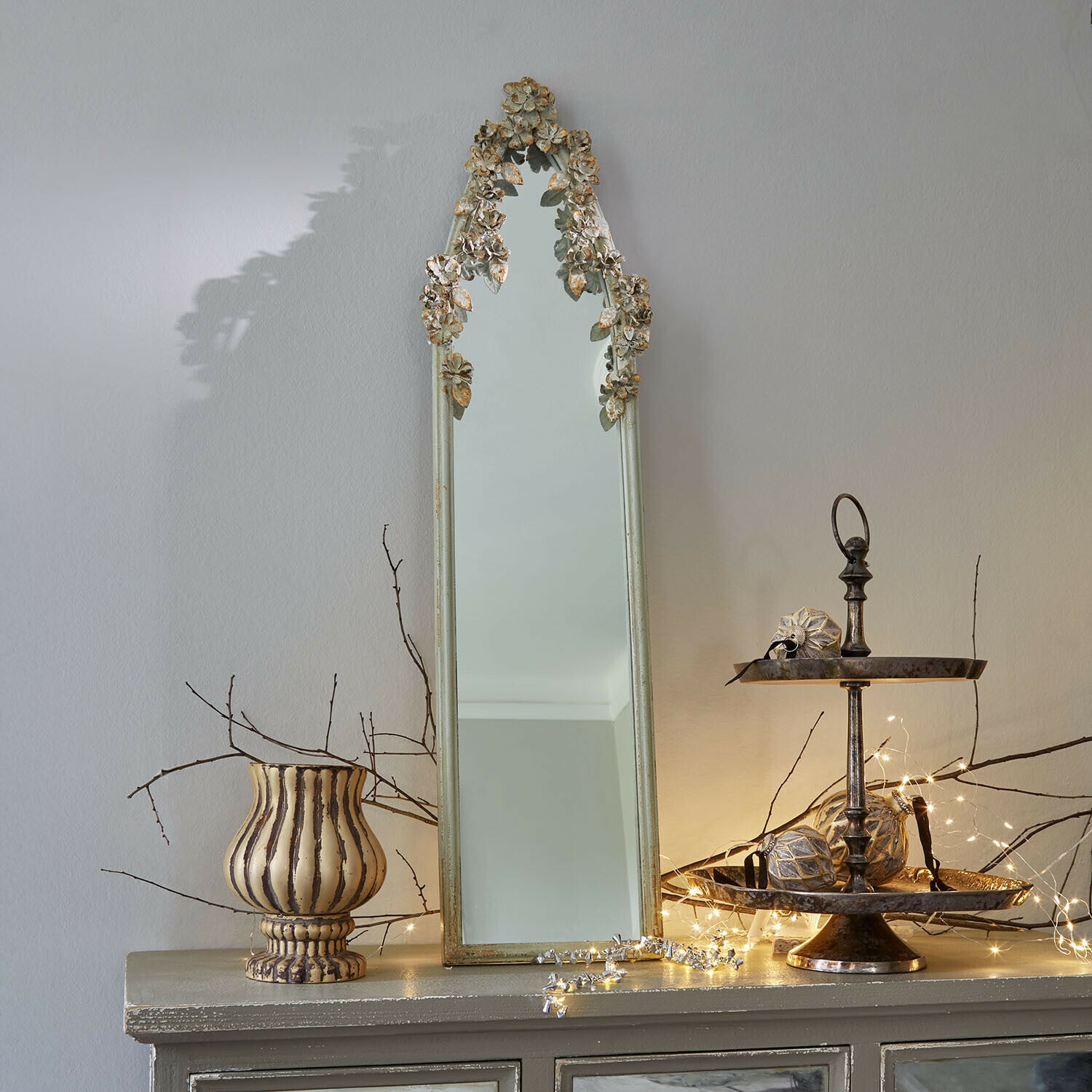 Spiegel Clarendons Smalle spiegel met antiek gouden lijst en bloemmotief op kast met decoraties en lichtjes