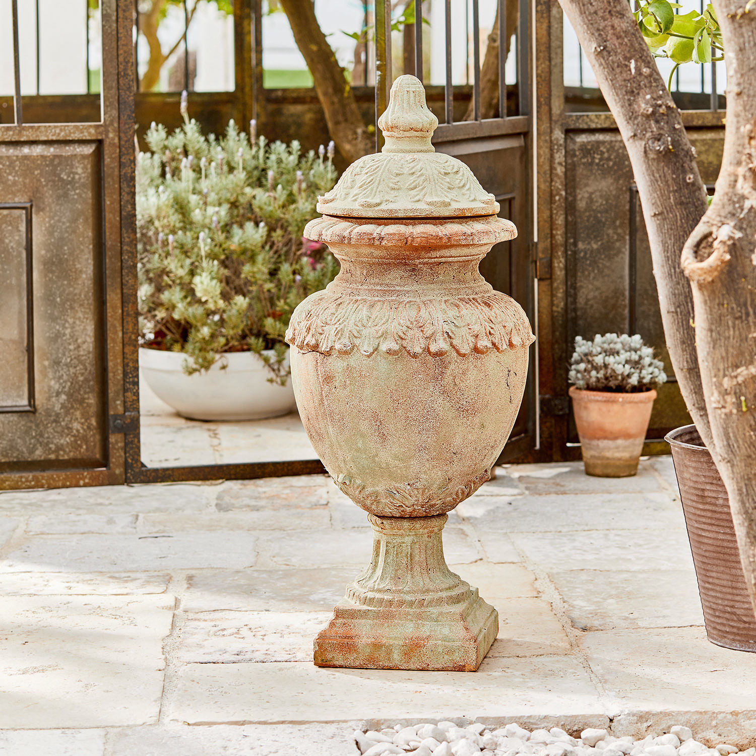 Siervoorwerp Persephone Decoratieve tuinvaas van terracotta in natuurlijke kleur op stenen vloer met planten op de achtergrond