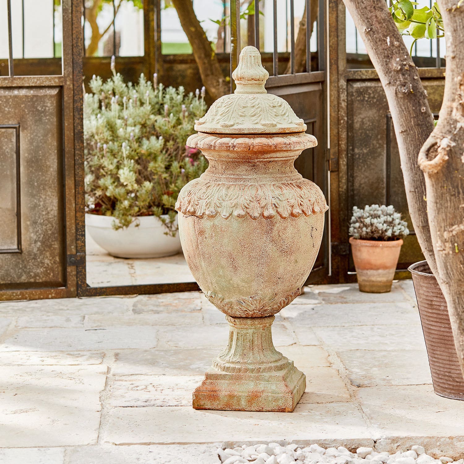 Siervoorwerp Persephone Decoratieve tuinvaas van terracotta in natuurlijke kleur op stenen vloer met planten op de achtergrond