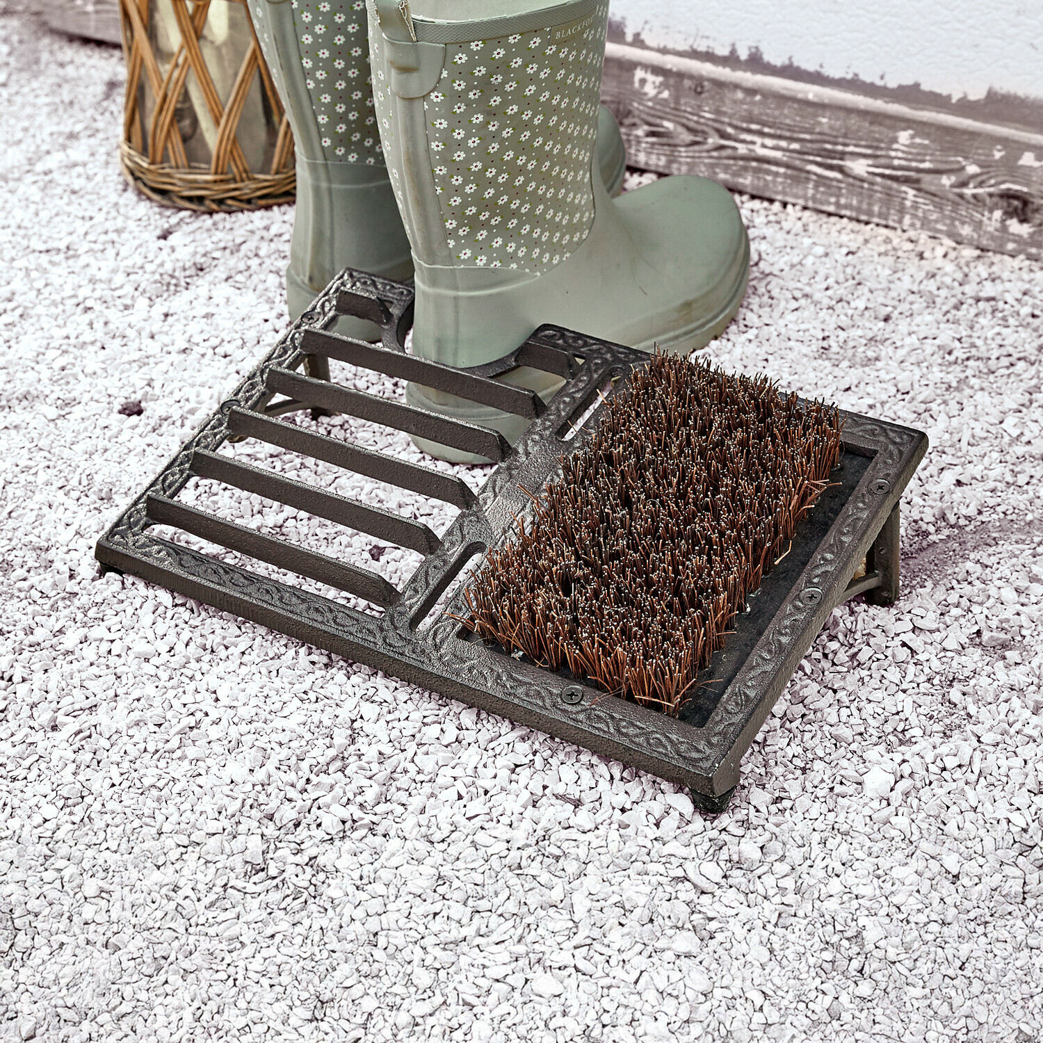 Zwarte gietijzeren schoenreiniger met harde borstel en laarshouder op grind