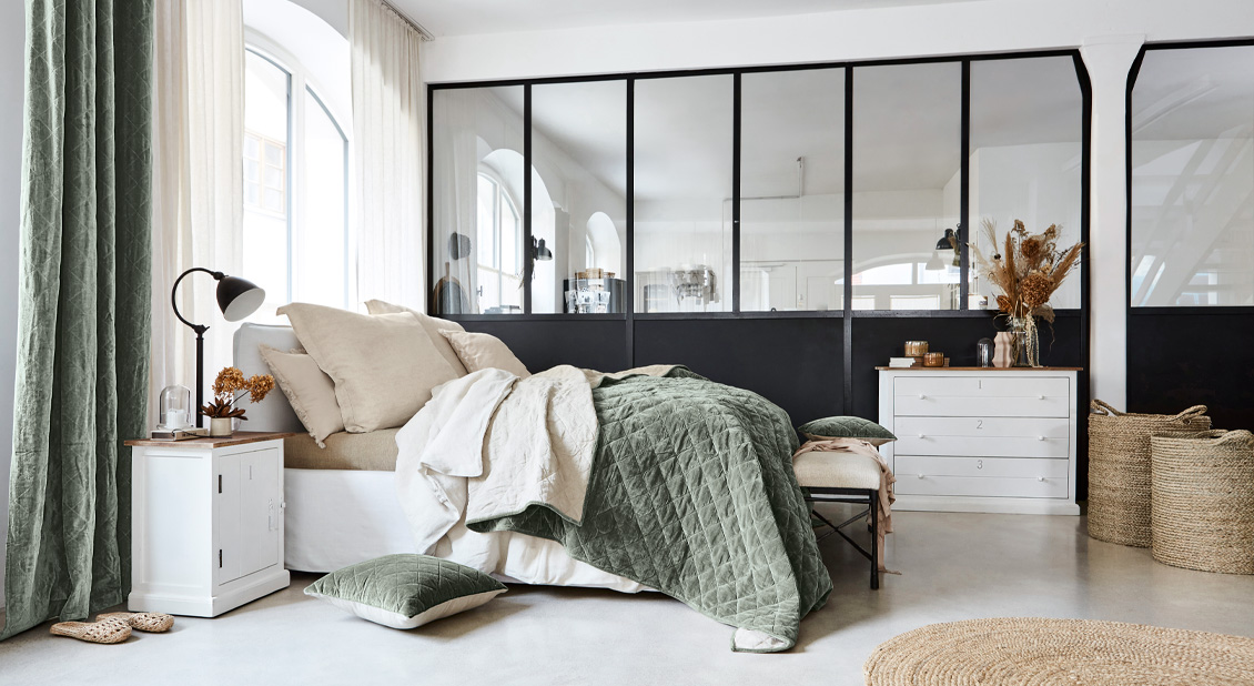 Gezellige slaapkamer met groen doorgestikt dekbed en natuurlijke decoraties in industriële stijl