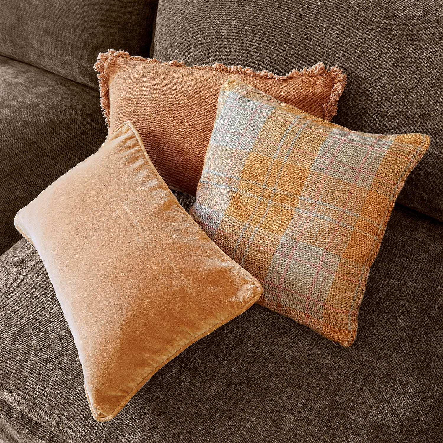 Drie decoratieve kussens in oranje tinten op een bruine bank voor een gezellige woonkamer