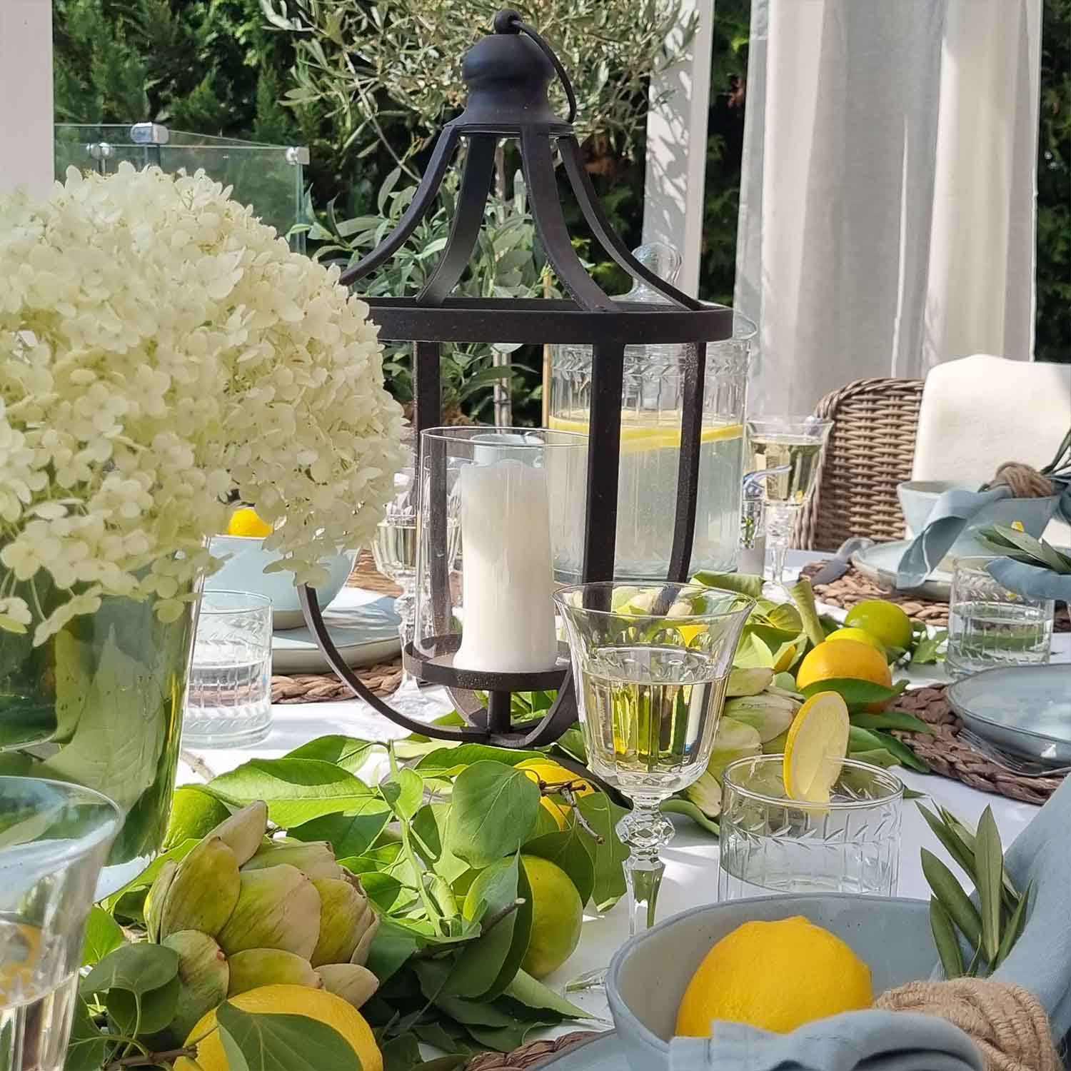 Zwarte metalen lantaarn met witte kaars op zomerse tafel met citroenen en groene bladeren