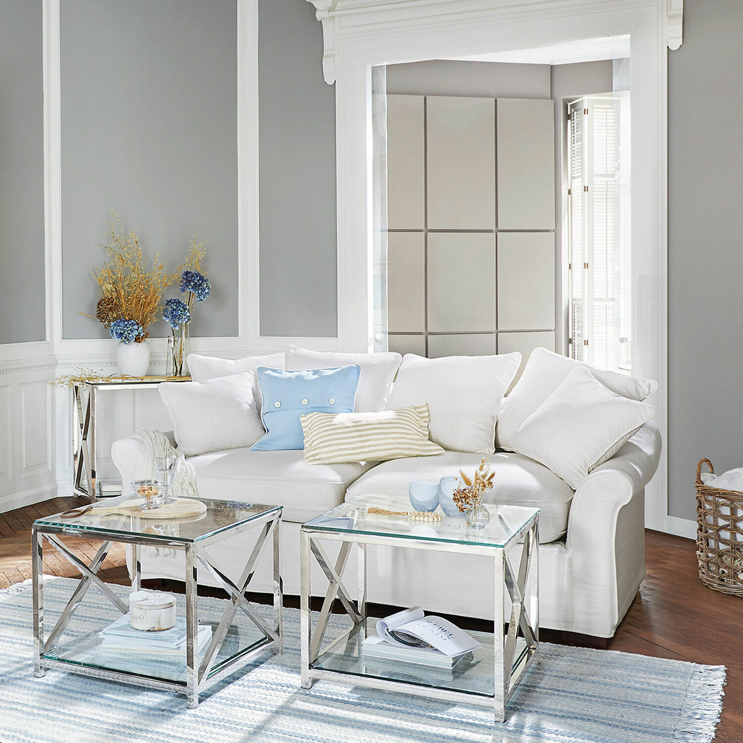 Moderne woonkamer met witte bank en twee glazen tafels met metalen frame op een lichtblauw tapijt