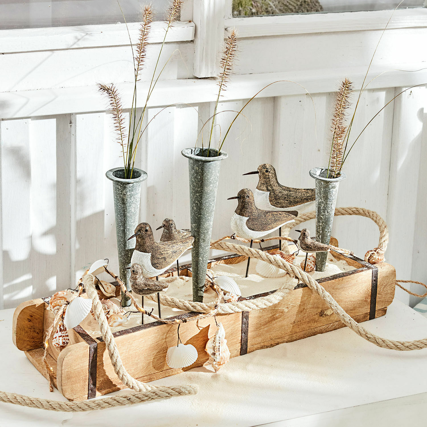 Decoratieve houten bak met metalen vazen, vogelornamenten en schelpen in maritieme stijl