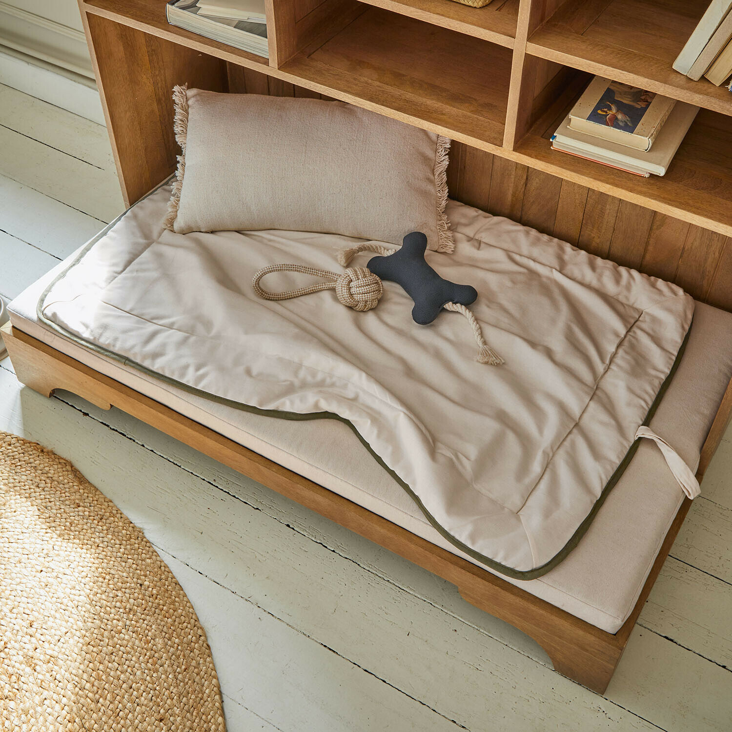 Beige hondenbed met kussen en speeltje op houten frame, comfortabele rustplek voor honden