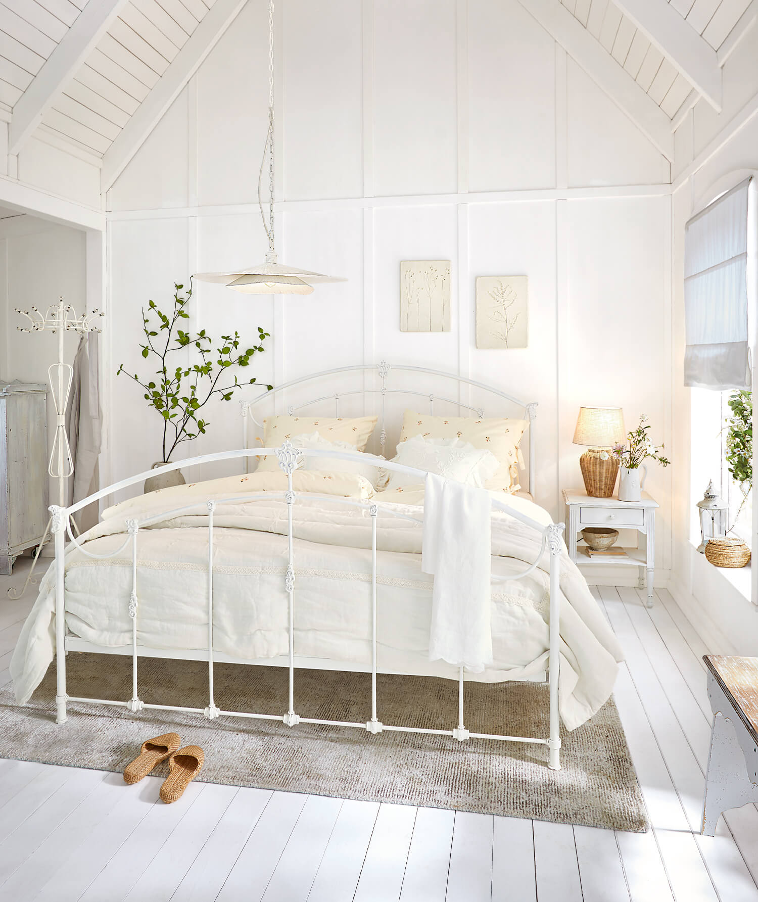 Wit metalen bedframe in lichte slaapkamer met crèmekleurig beddengoed en natuurlijke vloerkleed