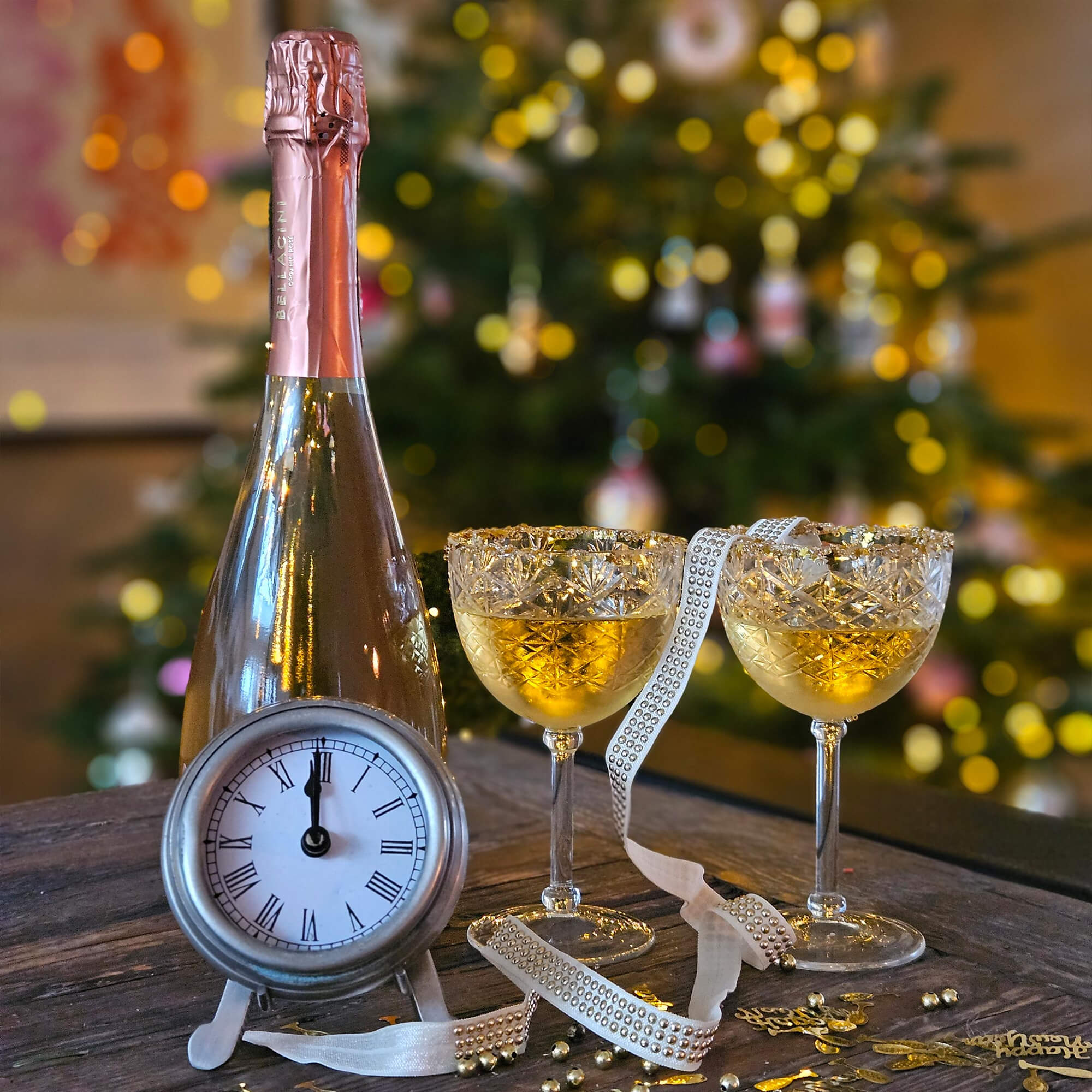 Fles champagne met roze folie, twee kristallen glazen met gouden drank en klok op houten tafel