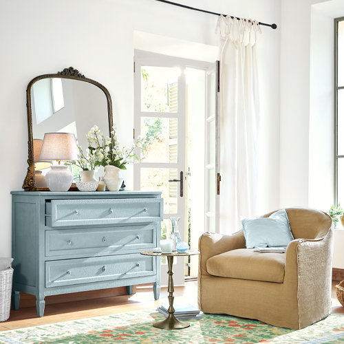 Lichtblauwe houten ladekast met spiegel en decoraties in lichte woonkamer met beige fauteuil