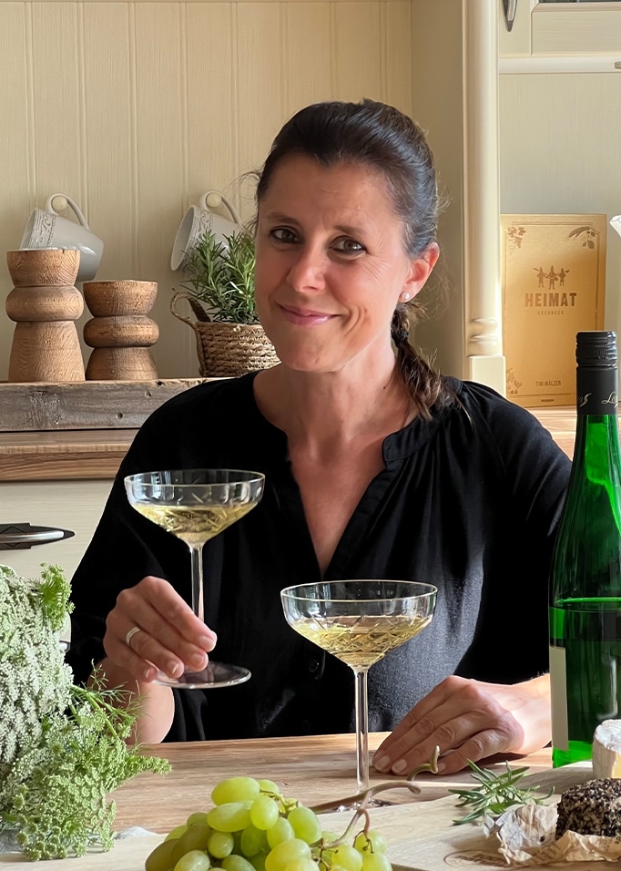 Vrouw in zwart overhemd met glas witte wijn aan tafel met druiven en kaas