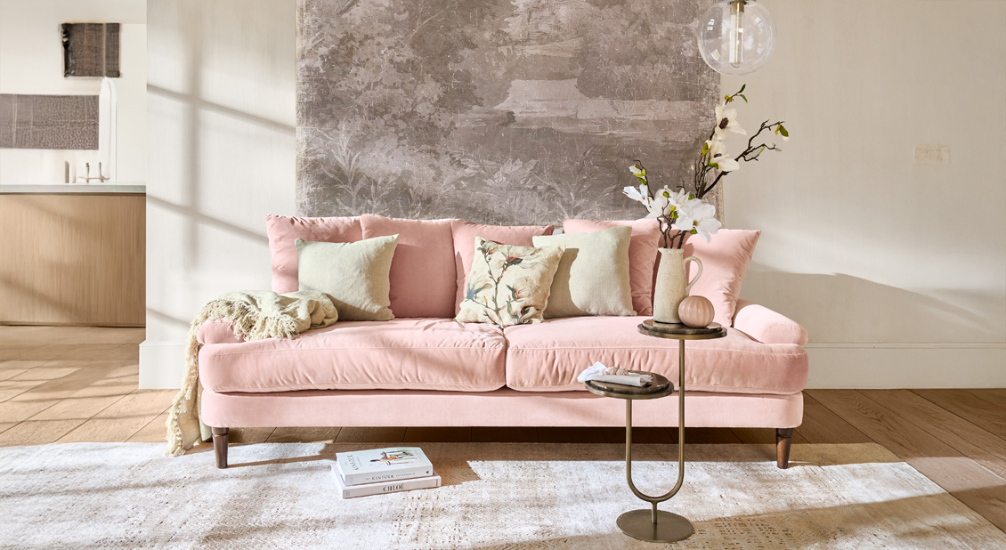 Roze fluwelen bank met kussens en bijzettafel in lichte, moderne woonkamer