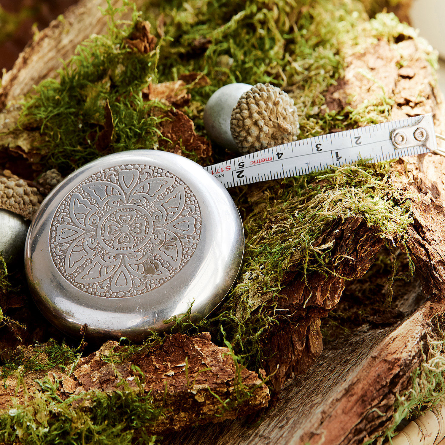 Meetlint Jesolo Metalen meetlint met bloemmotief op mosbedekt hout, praktisch meetinstrument